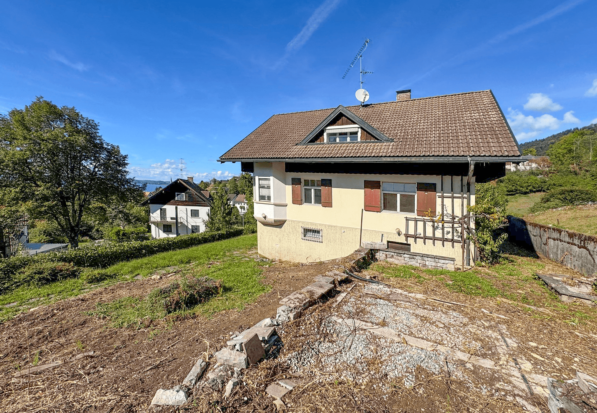 Haus auf einem Hanggrundstück mit Blick auf den See in der Ferne und vorbereitetem Gelände.