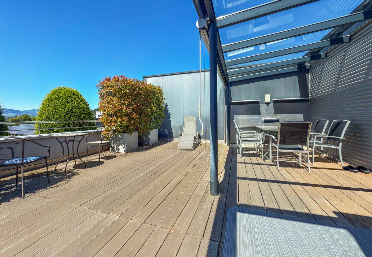 Große Holzterrasse mit Glasüberdachung, Gartenmöbeln und Pflanzen.