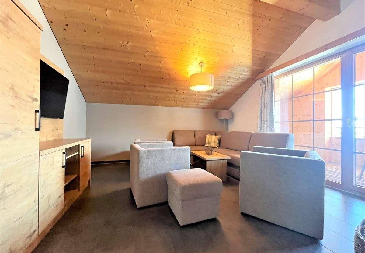 Gemütliches Wohnzimmer mit bequemer Sitzecke, Holzbalkendecke und großen Fenstern für viel Tageslicht.