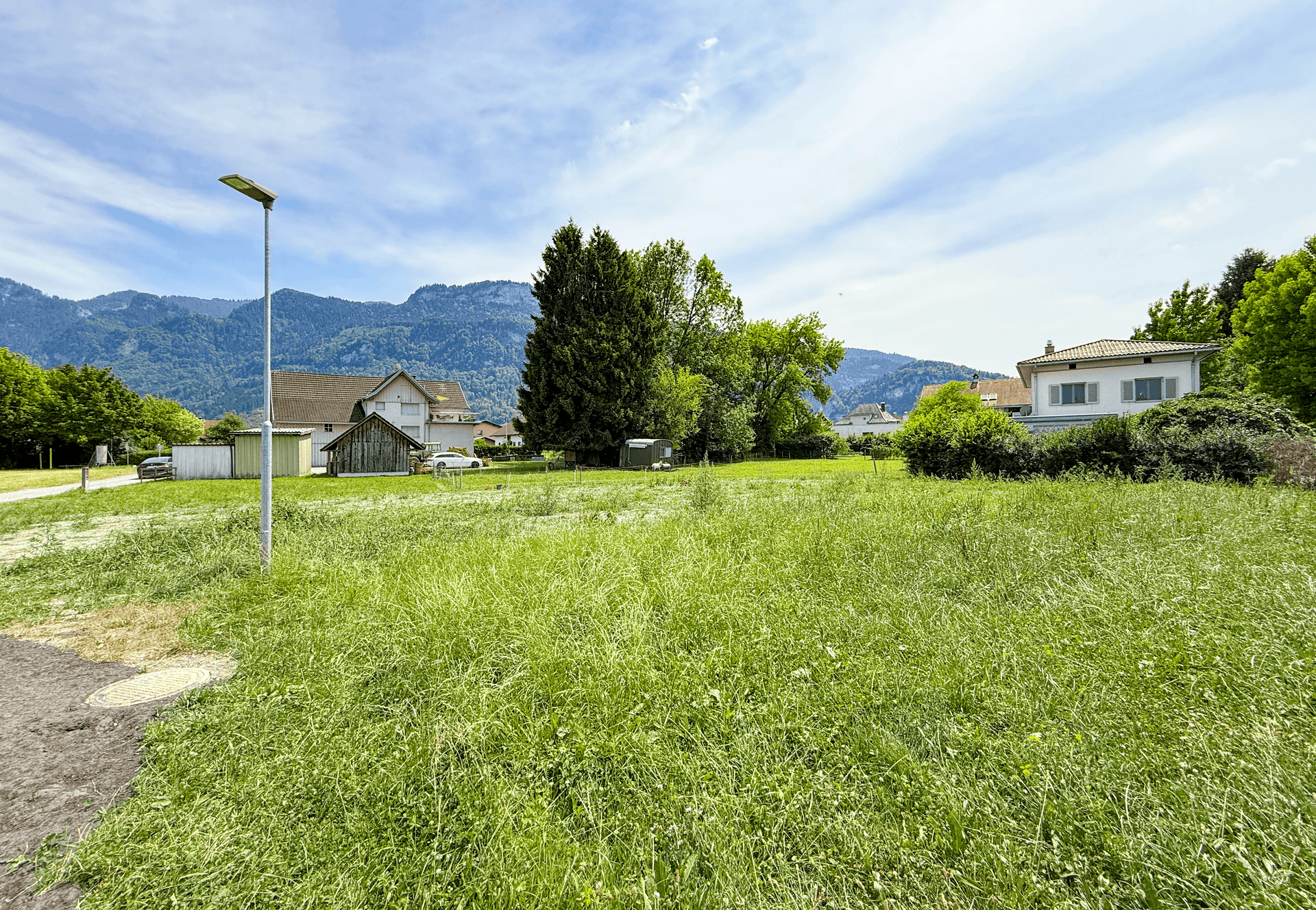 Offenes, grünes Grundstück mit einer Straßenlaterne und malerischem Blick auf die Berge.
