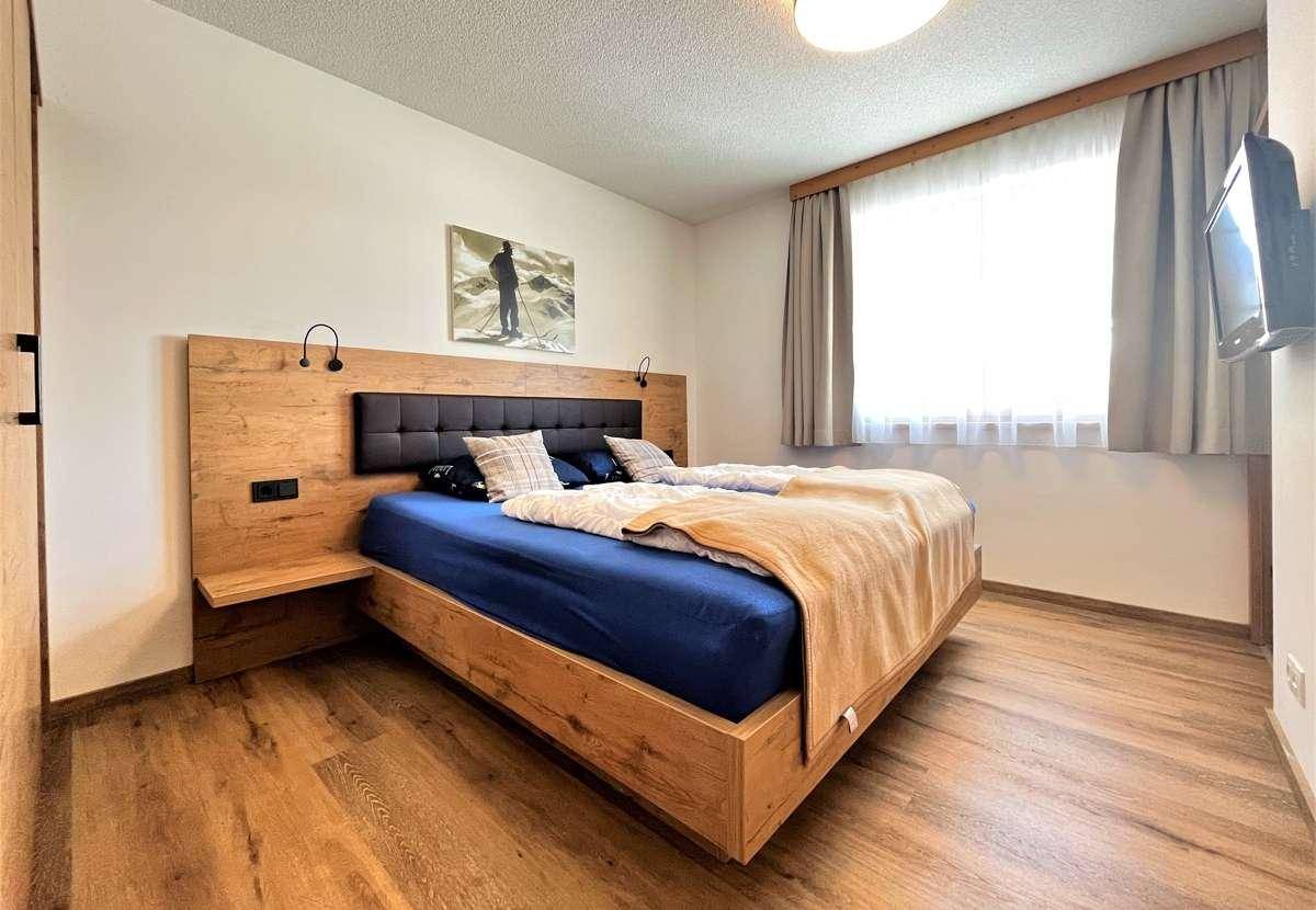 Modernes Schlafzimmer mit Holzbett, Nachttischen und großem Fenster.
