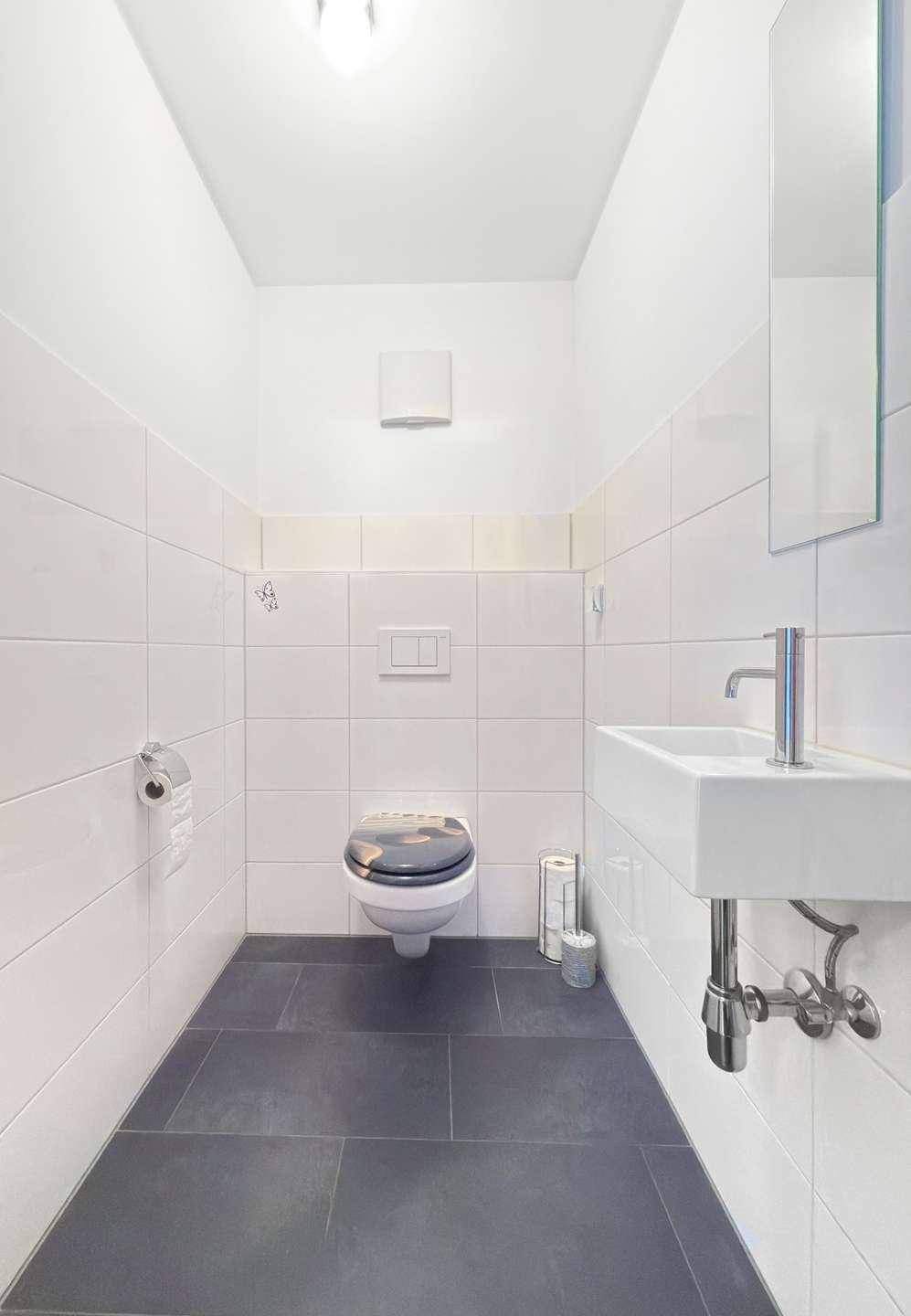 Modernes Gäste-WC mit Wand-WC, kleinem Waschbecken und dunklen Bodenfliesen.