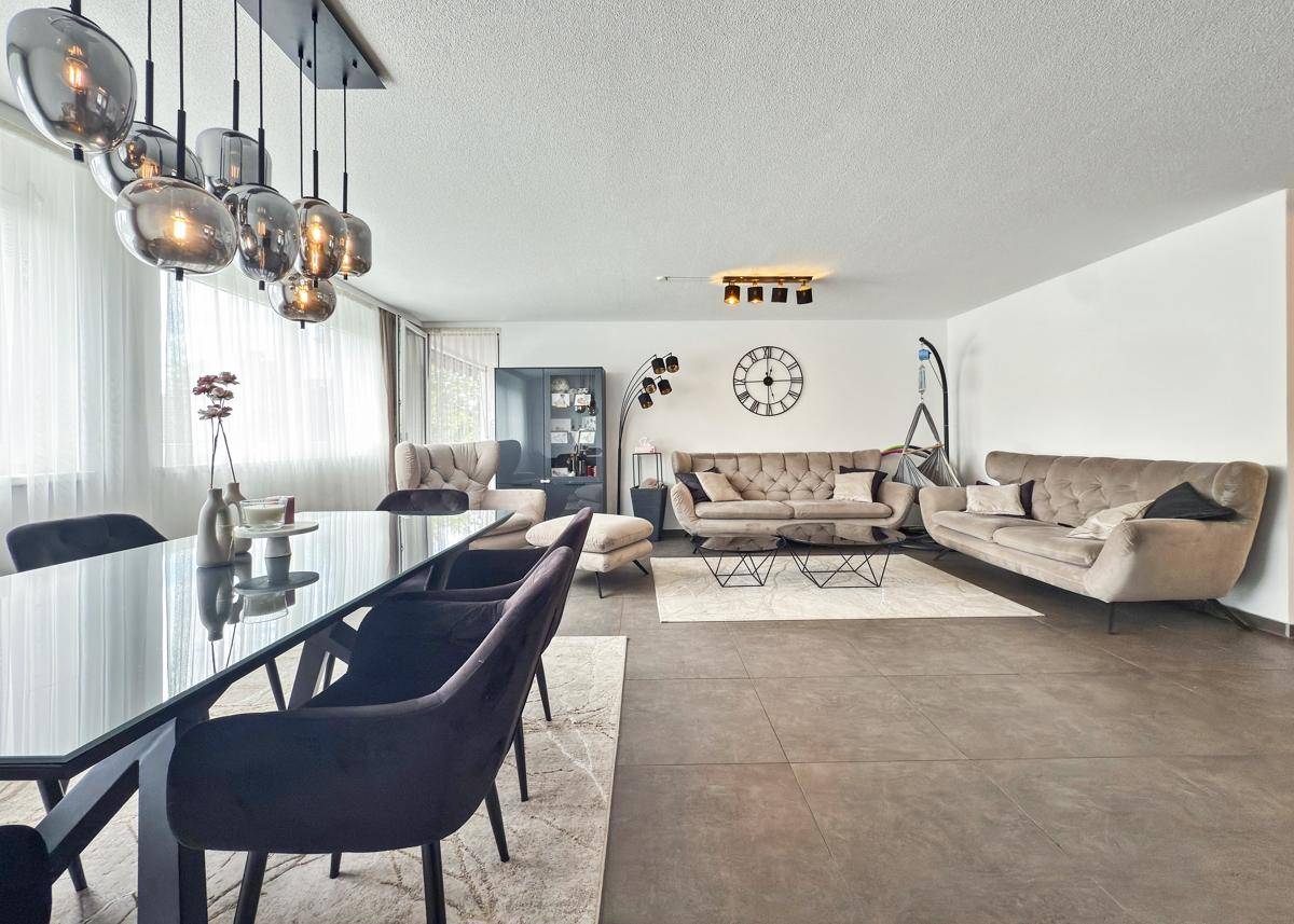 Stilvoller Wohn-Essbereich mit dunklem Esstisch, beigen Sofas und dekorativer Wanduhr.