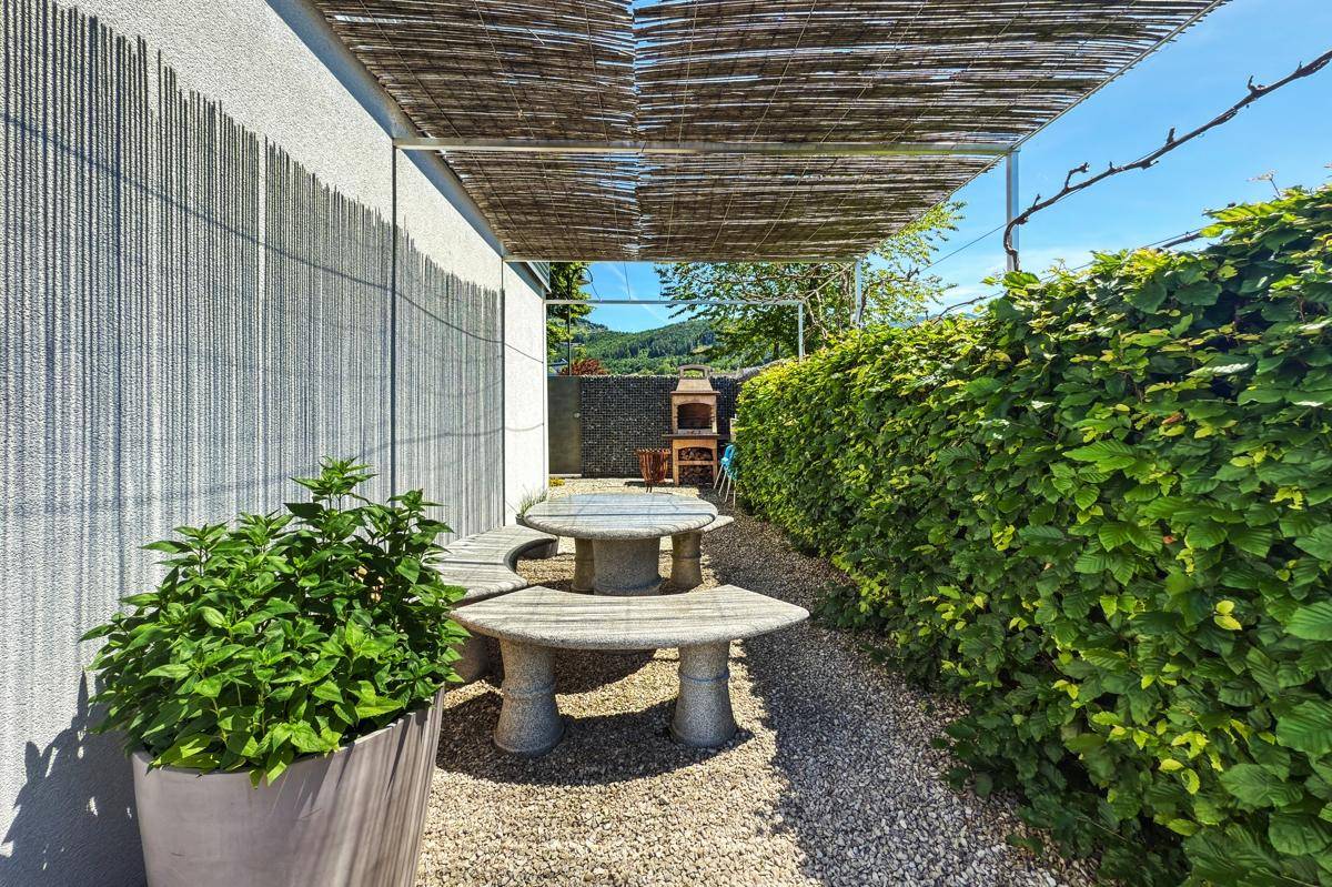 Gemütlicher Gartenbereich mit Steintisch, Sitzbänken und einer Pergola.