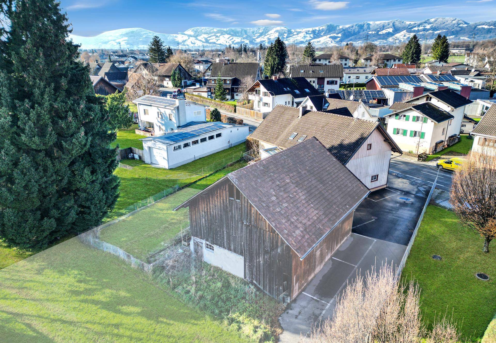 Luftaufnahme eines Wohngebiets mit einem Holzgebäude und schneebedeckten Bergen im Hintergrund.