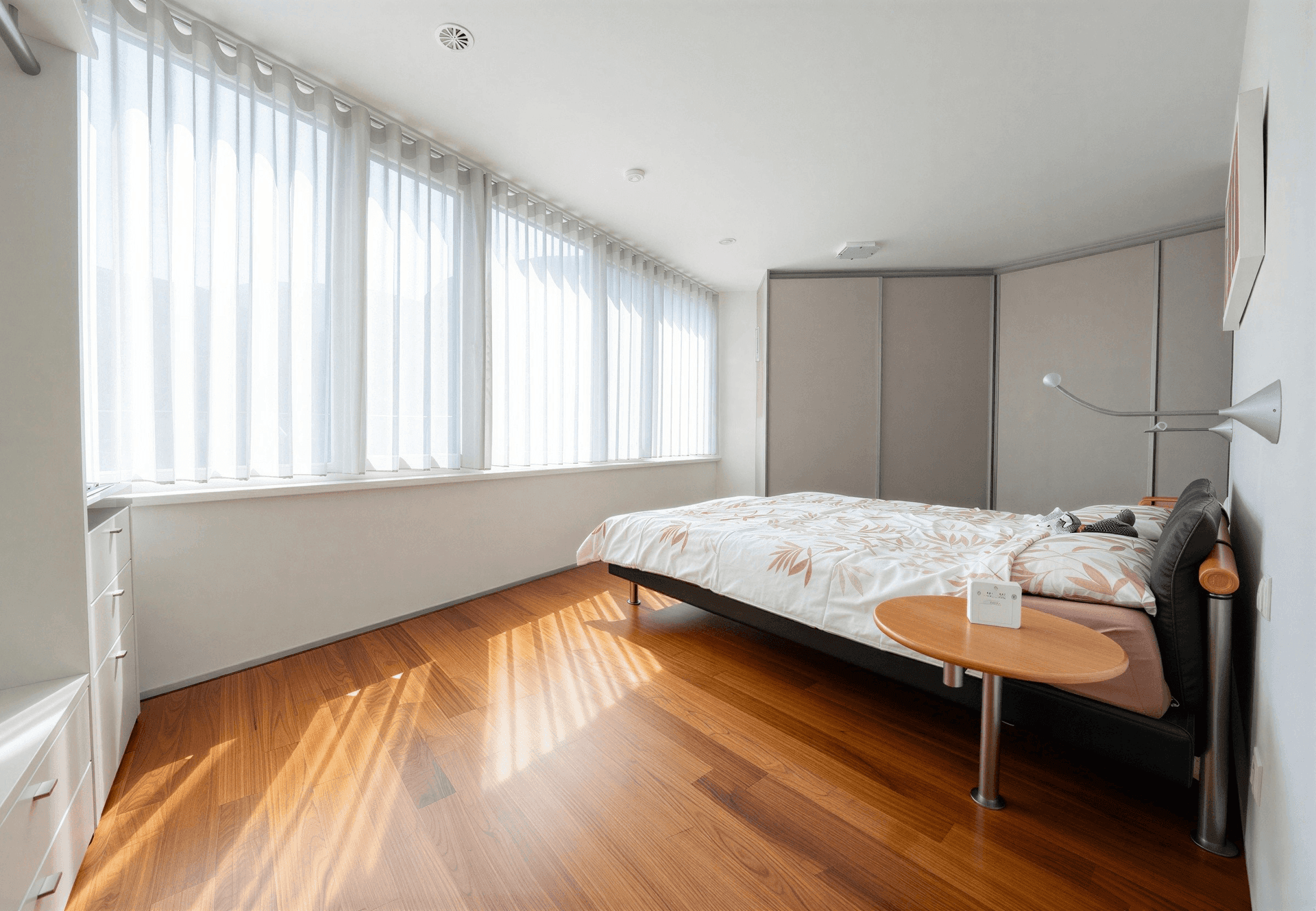 Helles Schlafzimmer mit großen Fenstern, Holzboden und Einbauschränken. Viel natürliches Licht fällt in den Raum.