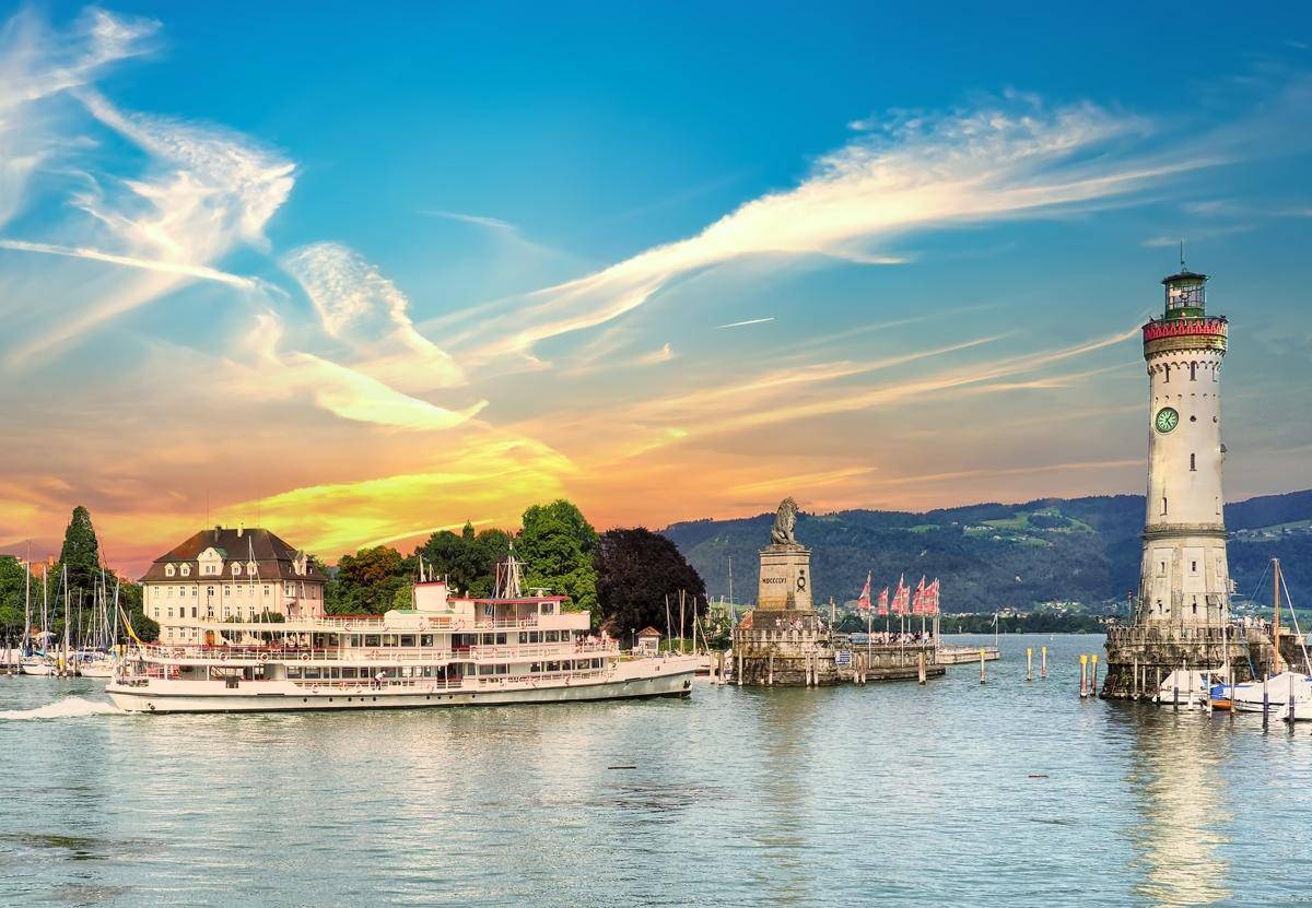 Ein Schiff fährt auf dem See, vorbei an einem Leuchtturm und der malerischen Hafenstadt.