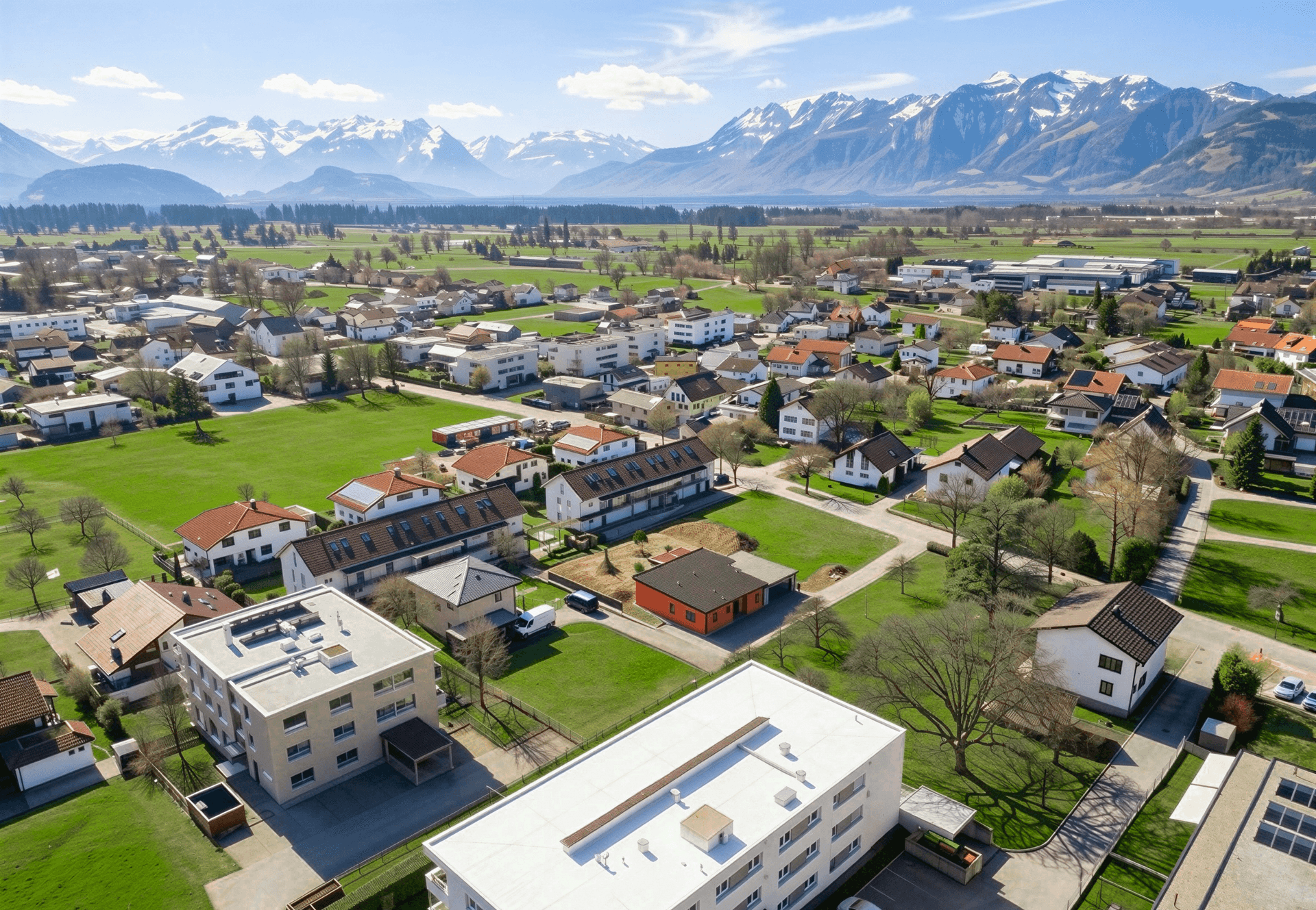 Weitwinkel-Luftaufnahme einer Siedlung mit Blick auf Berge und einen See in der Ferne.
