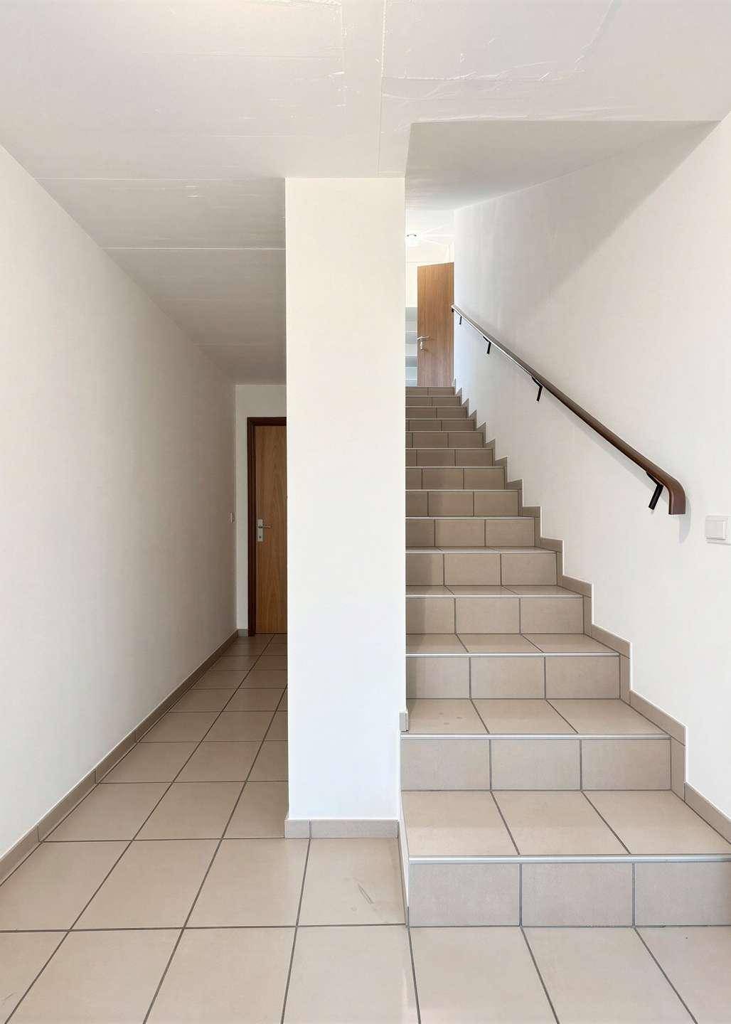 Heller Flur mit gefliester Treppe und schlichten weißen Wänden.