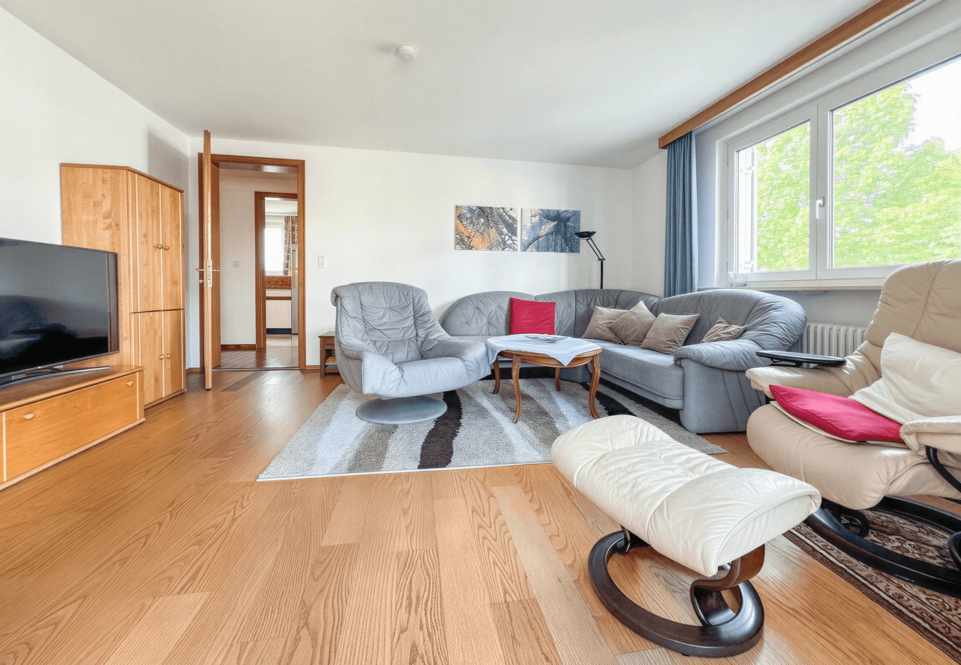 Gemütliches Wohnzimmer mit bequemen Sofas, Holzboden und Blick ins Grüne durch das Fenster.