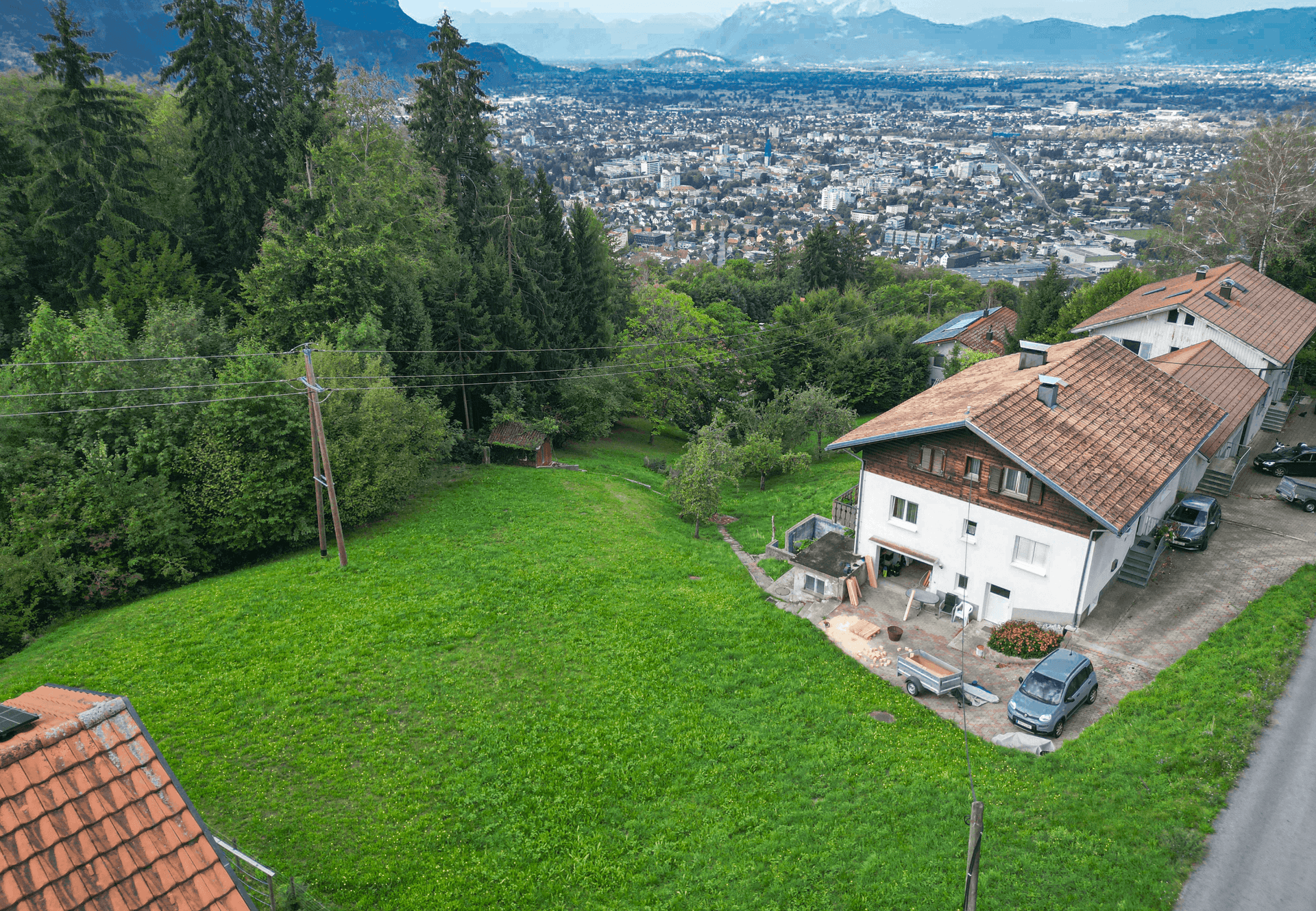 Panoramablick auf Wohnhäuser, grüne Wiesen und eine weitläufige Stadtlandschaft mit Bergen am Horizont.