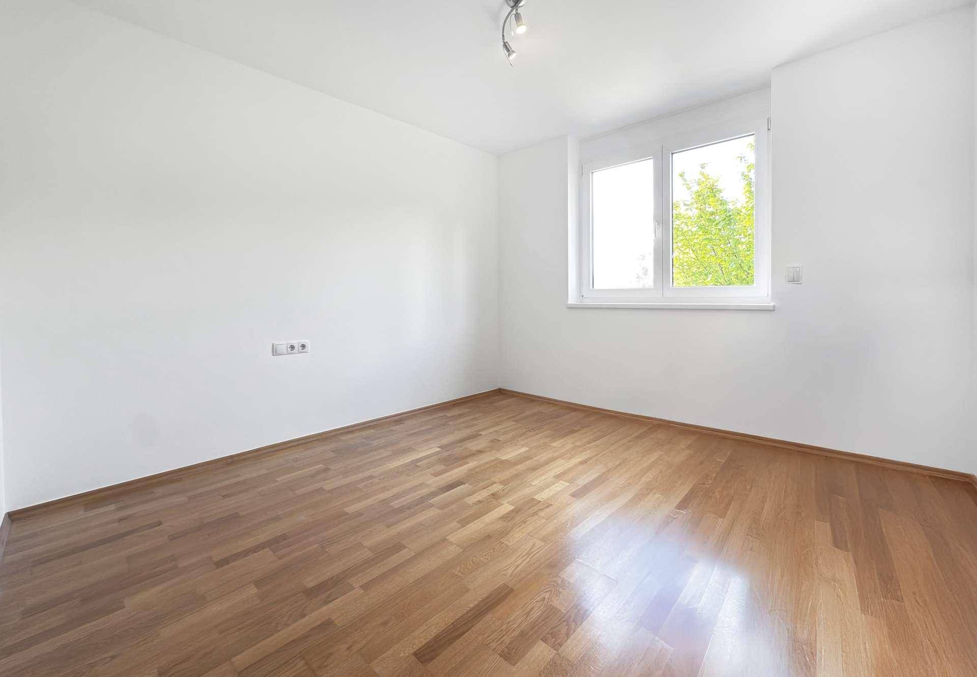 Leeres Zimmer mit Holzboden und hellem Fenster, ideal als Schlaf- oder Arbeitszimmer.
