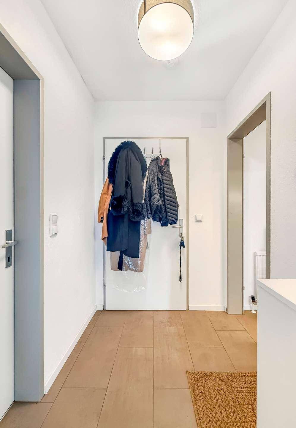 Heller Flur mit Fliesenboden und Garderobe, bietet Zugang zu den Zimmern.