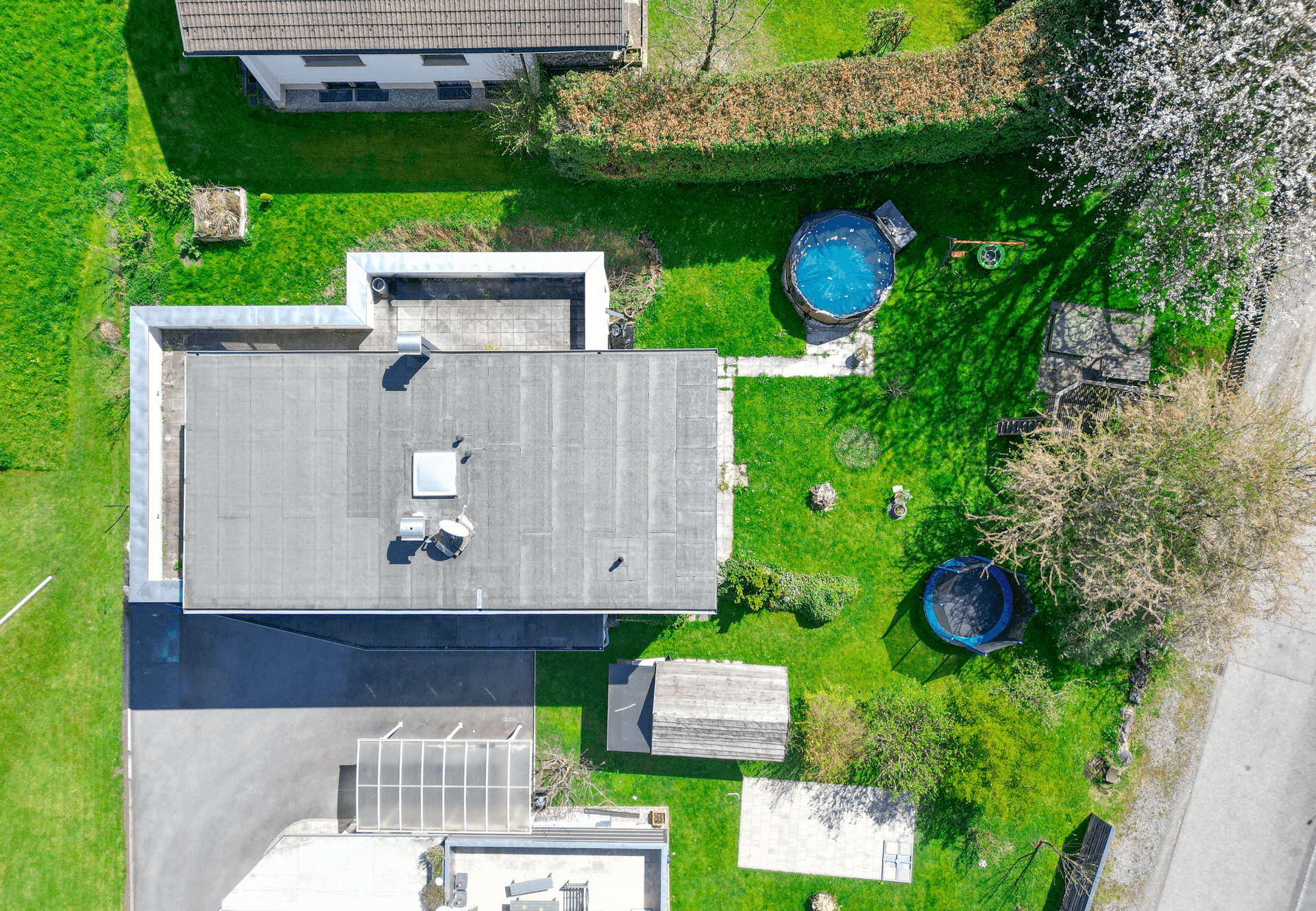 Luftaufnahme des Anwesens mit Flachdach, Garten, Pool und Carport.