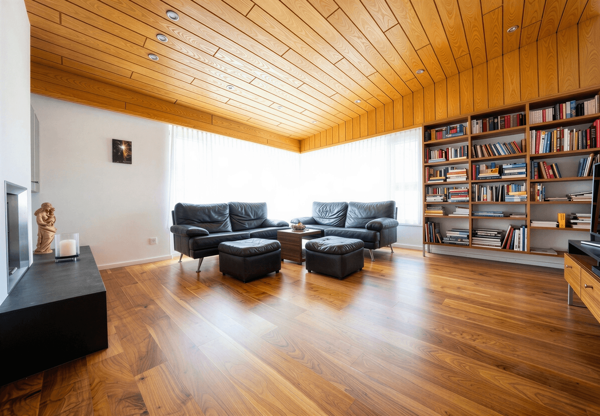 Geräumiges Wohnzimmer mit Holzbalkendecke, dunklen Ledersofas und großem Bücherregal.