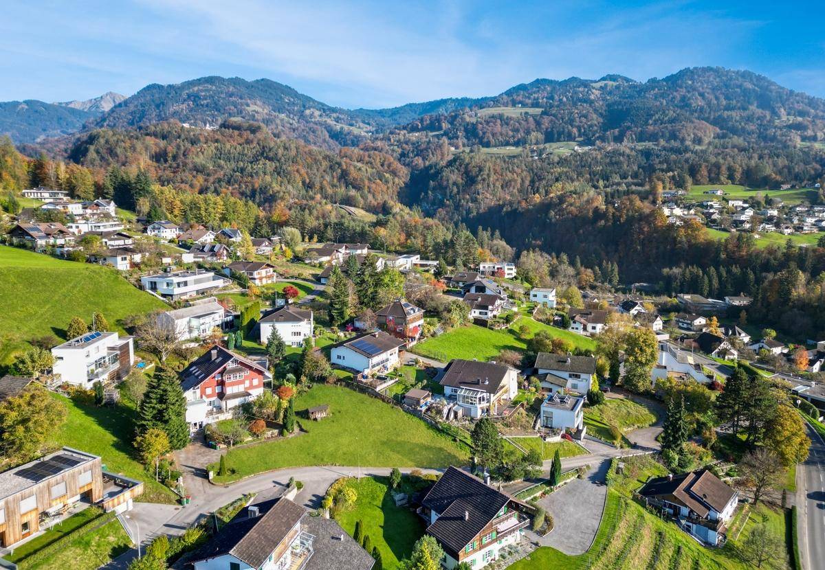 Weitläufige Wohngegend eingebettet in eine grüne Hügellandschaft mit dichtem Wald und Bergen.