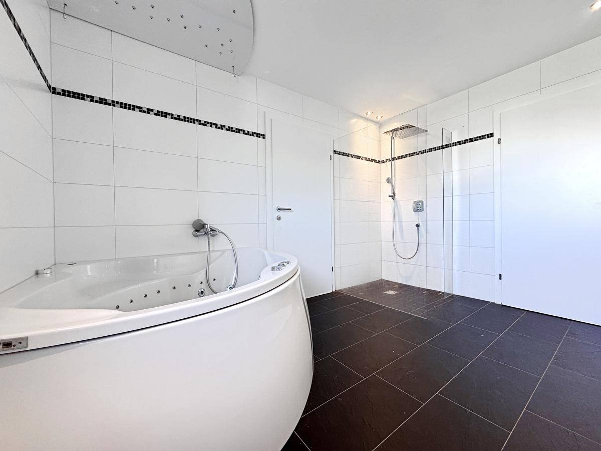 Modernes Badezimmer mit Whirlpool-Badewanne, großer Dusche und dunklen Bodenfliesen.