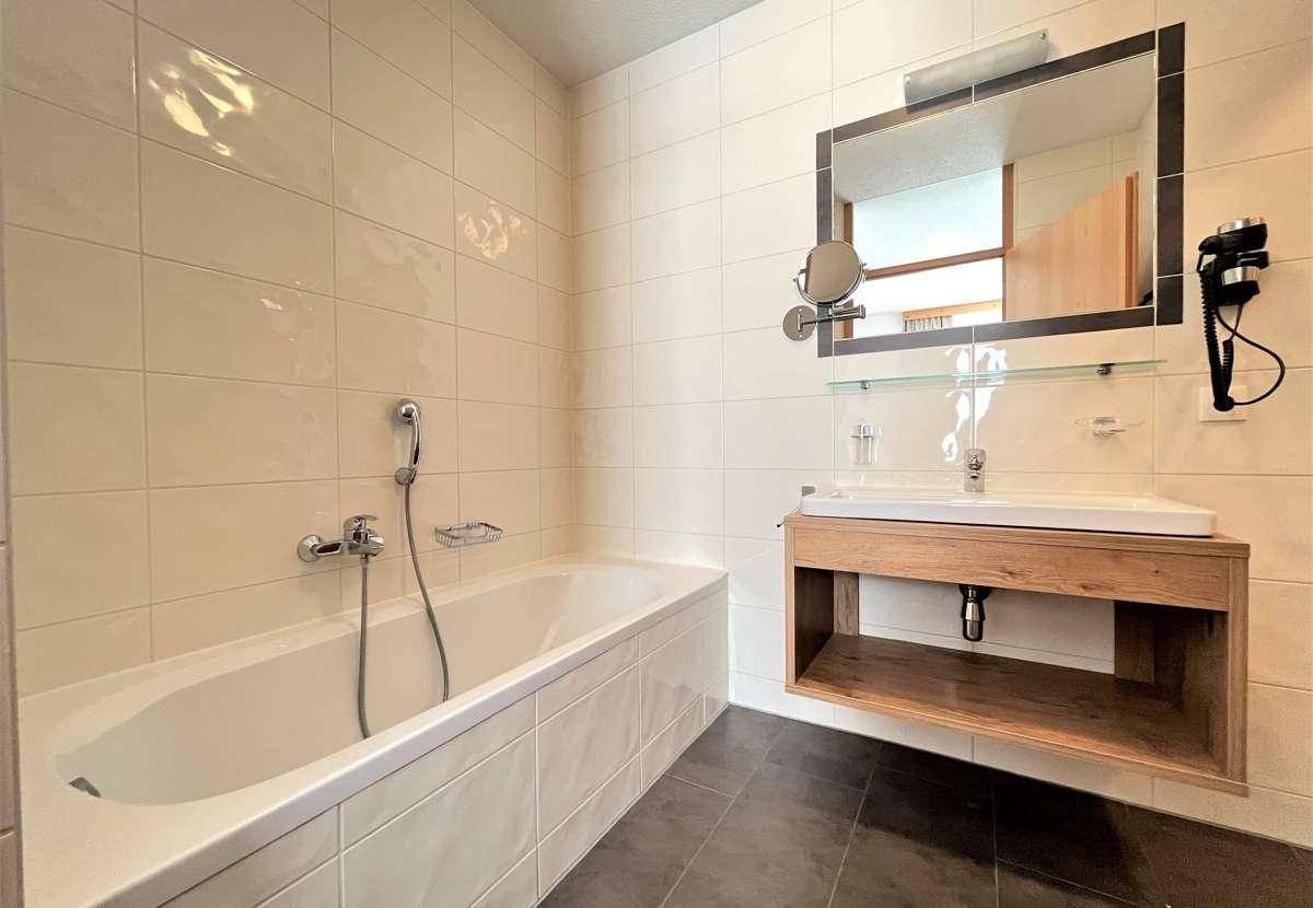 Helles Badezimmer mit Badewanne, Waschbecken und großem Spiegel.