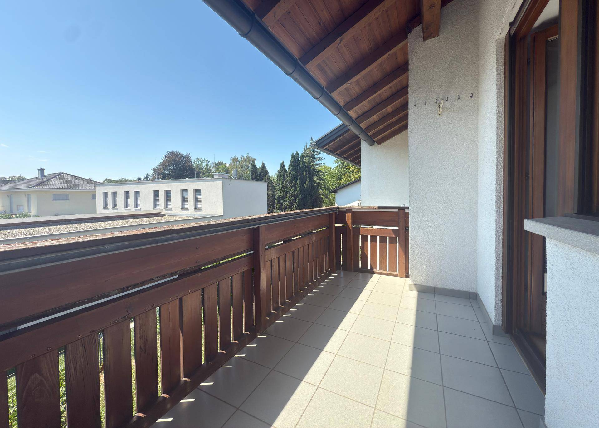 Balkon mit Fliesenboden und Holzbalkongeländer unter blauem Himmel.