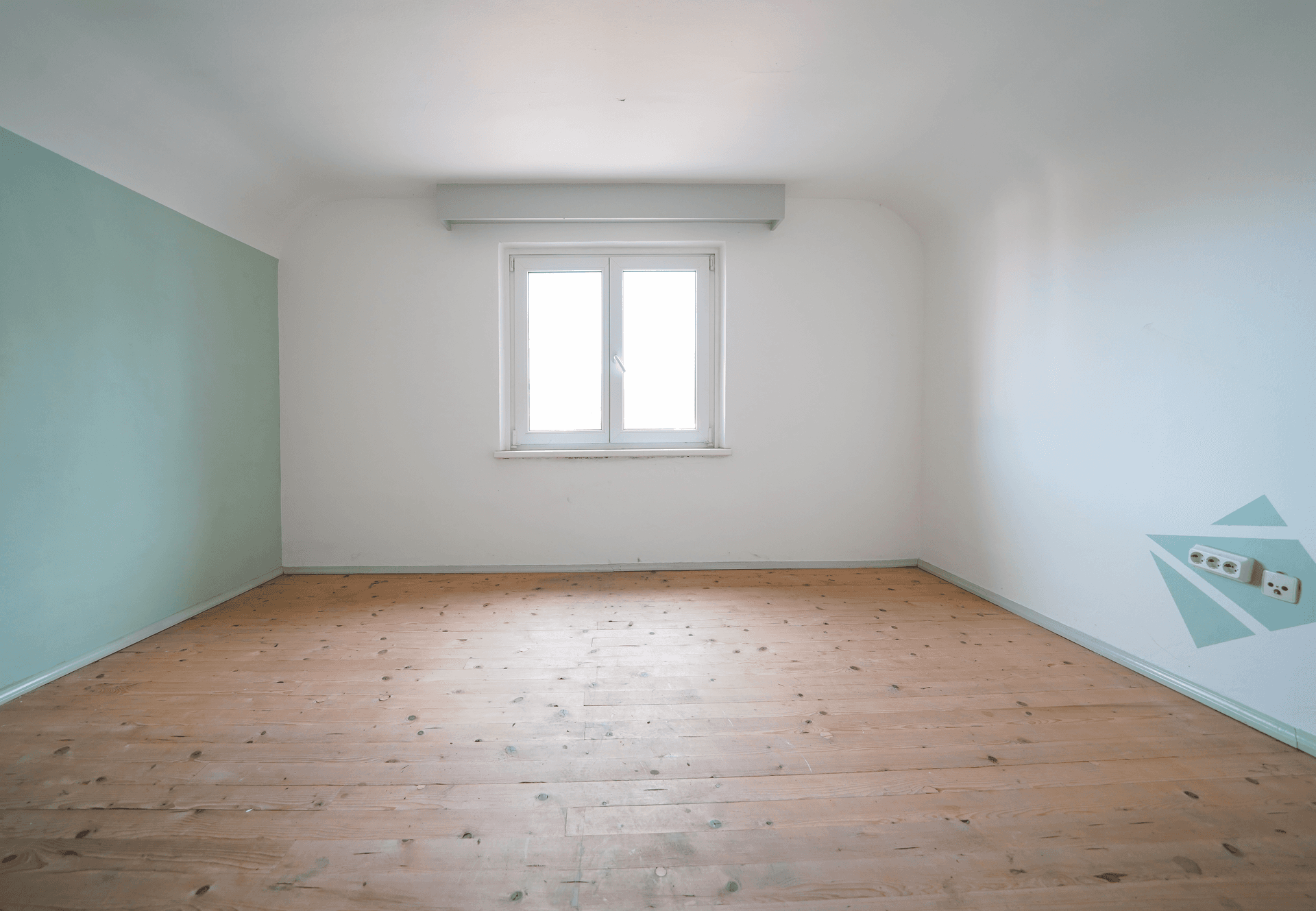 Leeres Zimmer mit hellem Holzfußboden, einem Fenster und einer mintgrünen Akzentwand mit Muster.