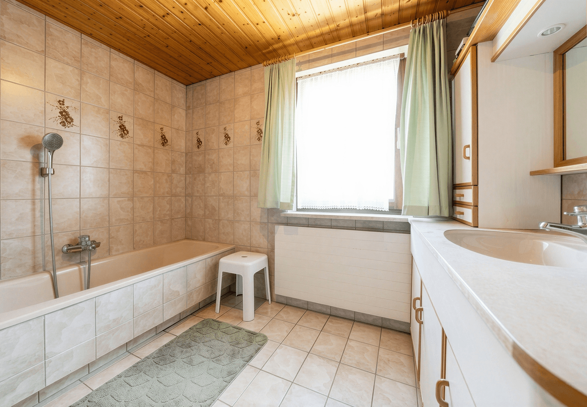 Badezimmer im 80er-Jahre-Stil mit Fliesen, Badewanne und Holzdecke.