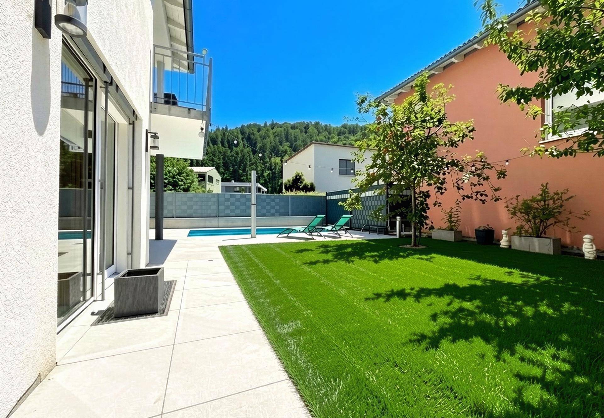 Gepflegter Garten mit Rasenfläche, Terrasse und Blick auf den Poolbereich.