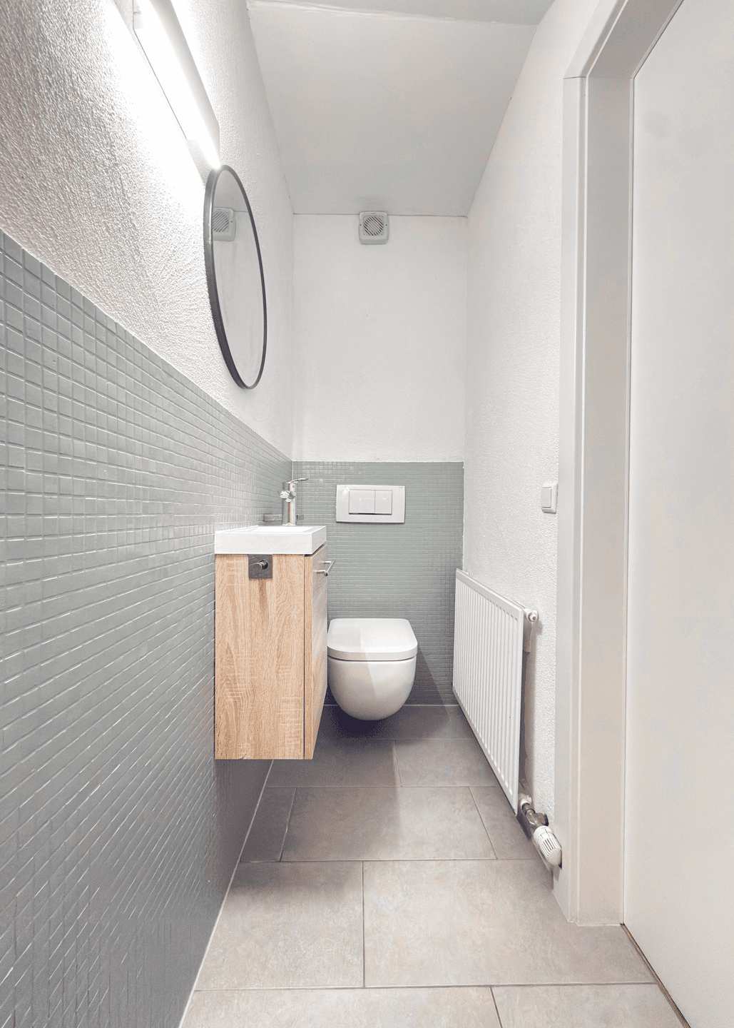 Modernes Gäste-WC mit Wand-WC, kleinem Waschbecken und grauen Mosaikfliesen.