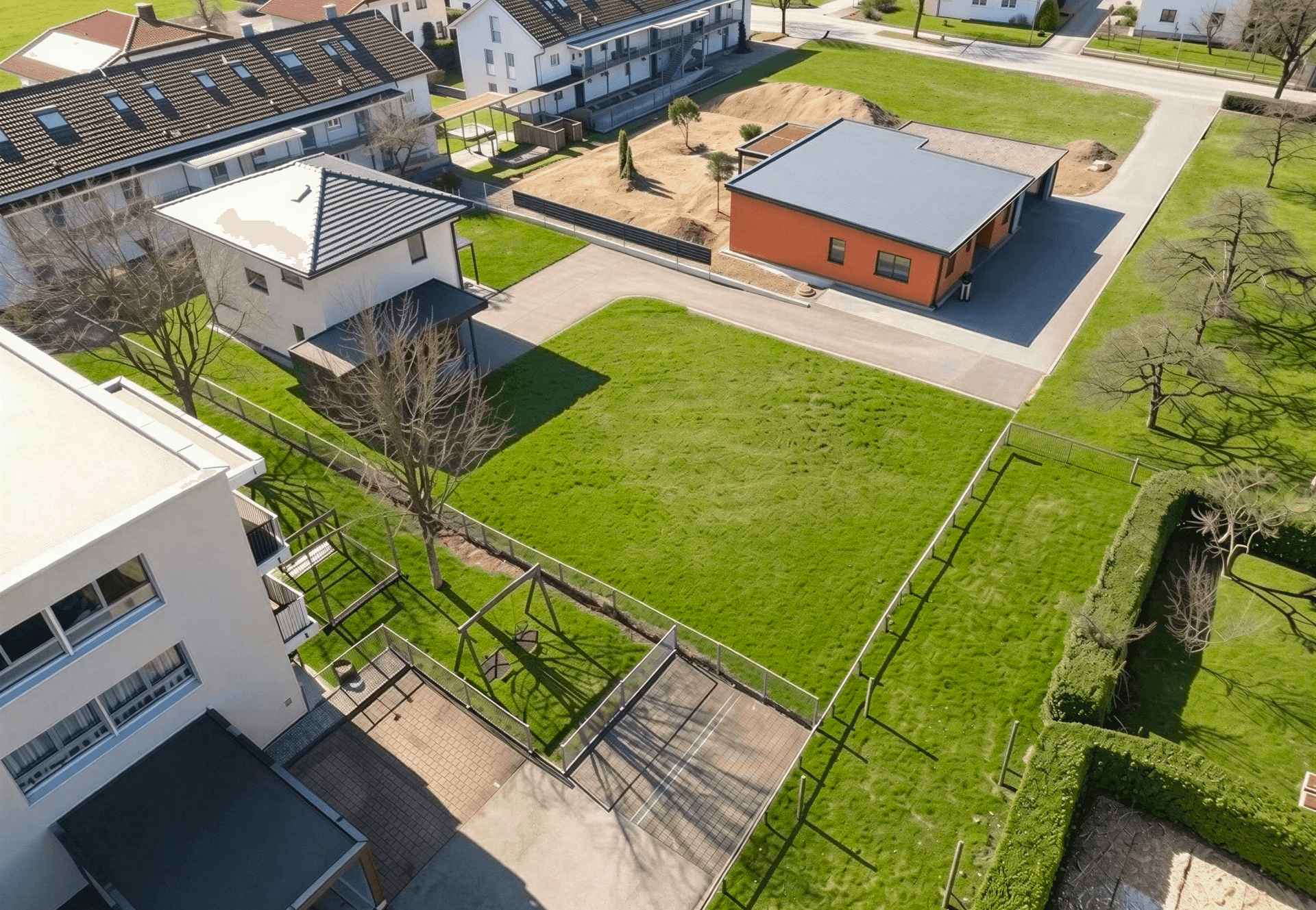 Blick von oben auf ein grünes Baugrundstück neben einem Spielplatz und modernen Gebäuden.