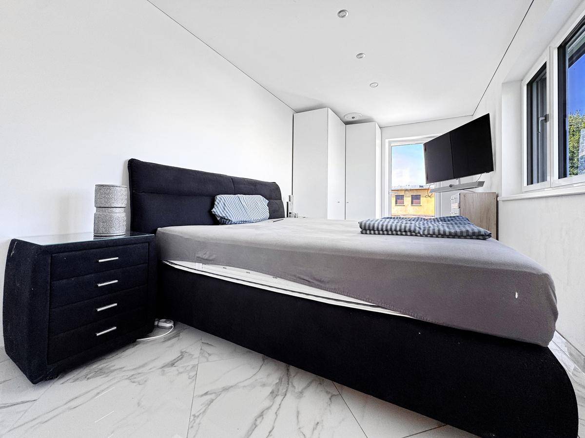 Modernes Schlafzimmer mit dunklem Bett, Marmorfliesen und großem Fenster.