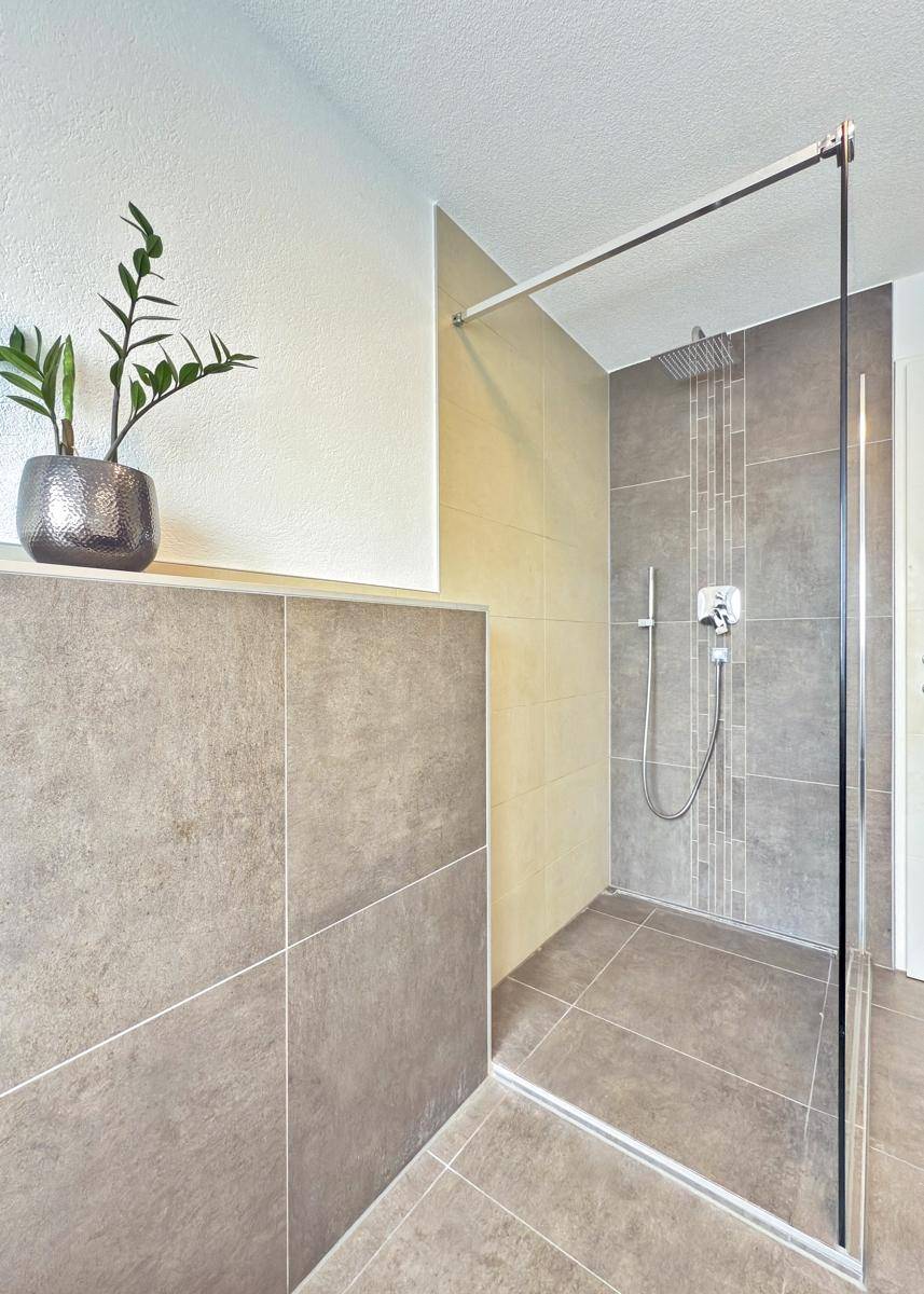 Ebenerdige Dusche im modernen Badezimmer mit grauen Wand- und Bodenfliesen.