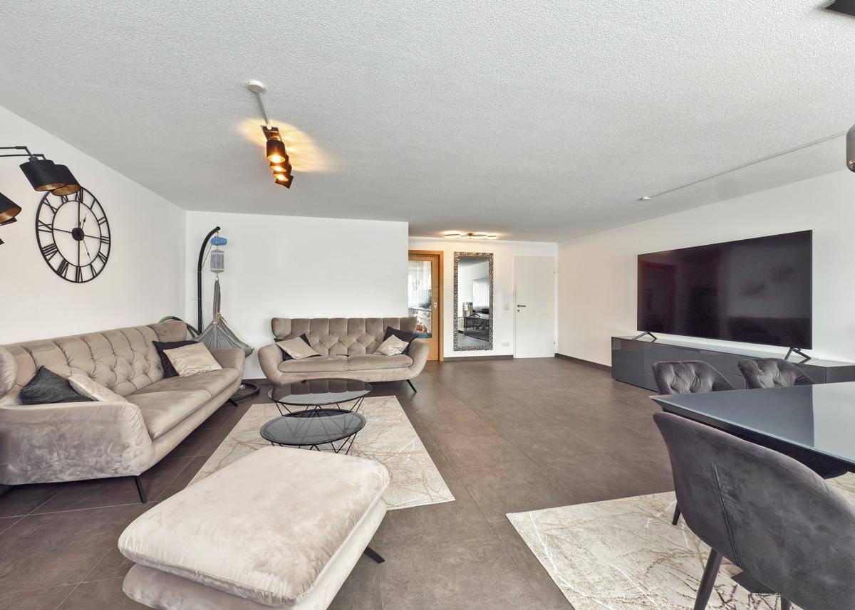 Moderner Wohn-Essbereich mit beigen Sofas, Fliesenboden und großem Fernseher.