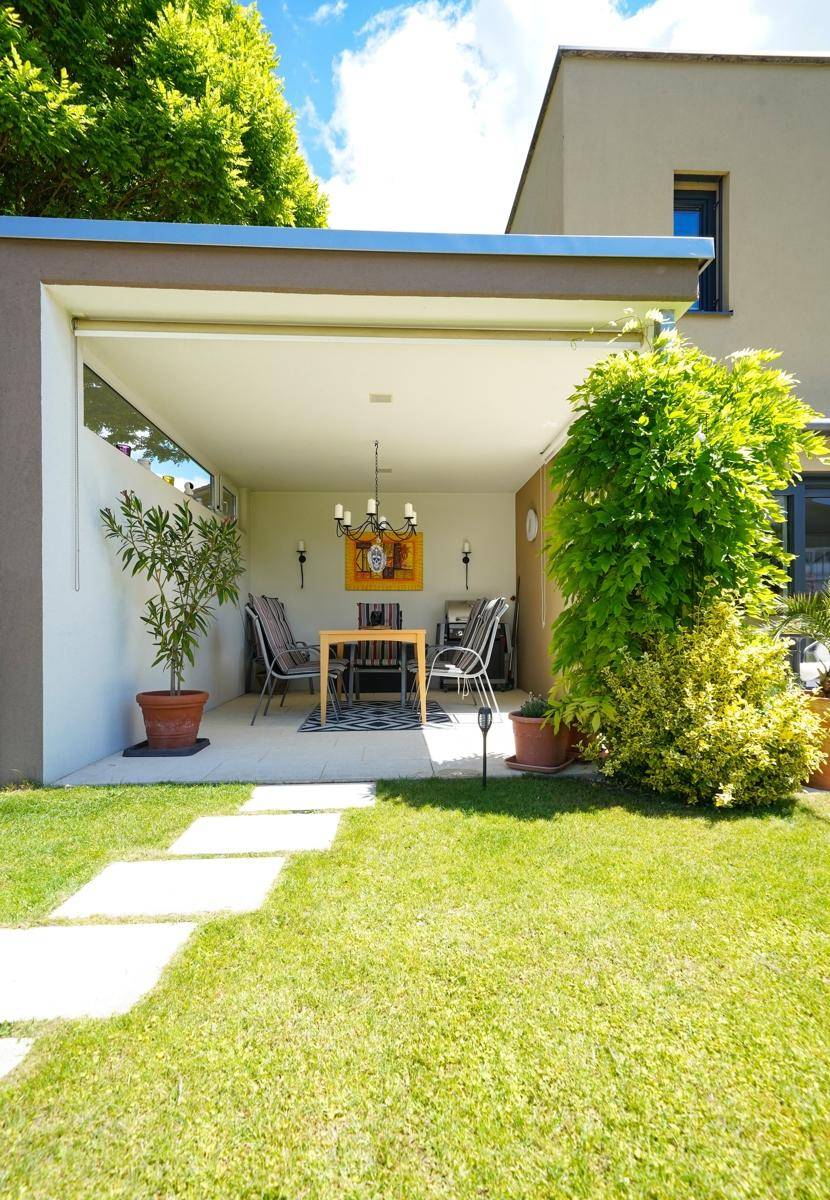 Überdachter Essbereich im Freien mit Tisch, Stühlen und Blick auf den Garten.