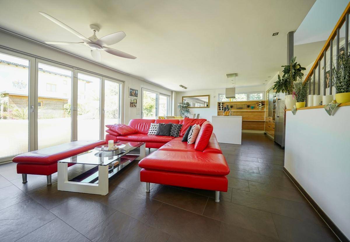 Geräumiger offener Wohnbereich mit rotem Sofa, großen Fenstern und Blick in den Garten.