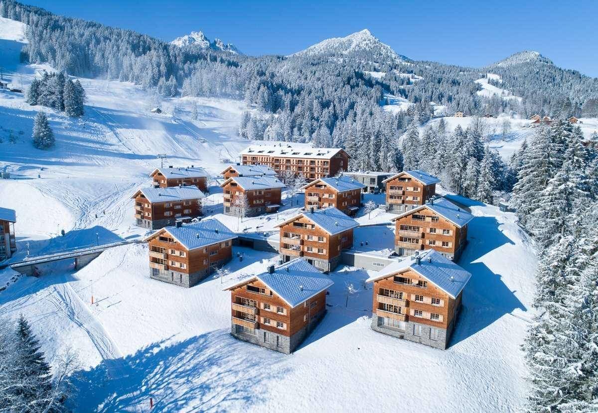 Idyllische Wohnanlage in einer verschneiten Berglandschaft mit klarem Himmel.