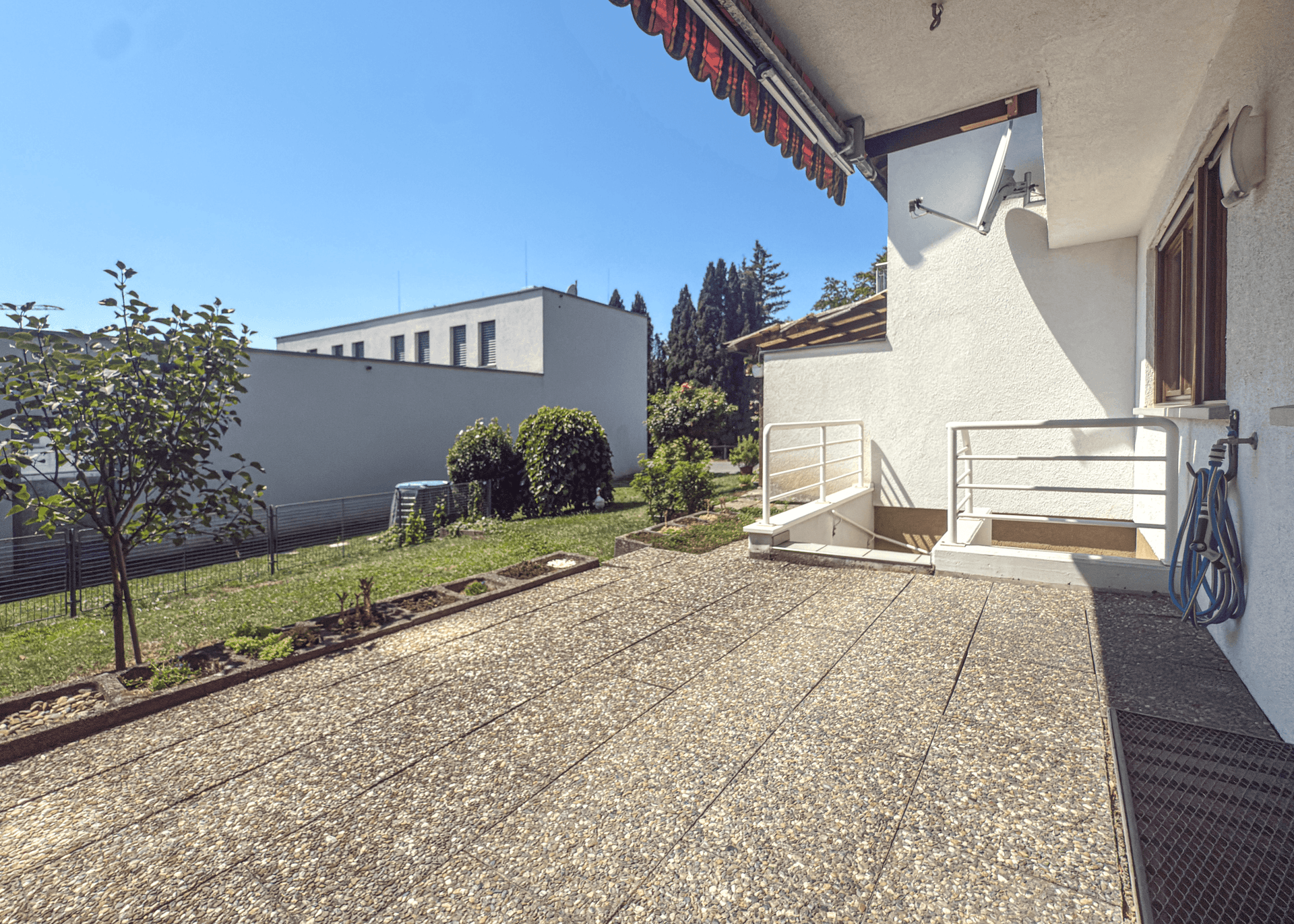 Große gepflasterte Terrasse mit Zugang zum Garten und Blick auf die Umgebung.