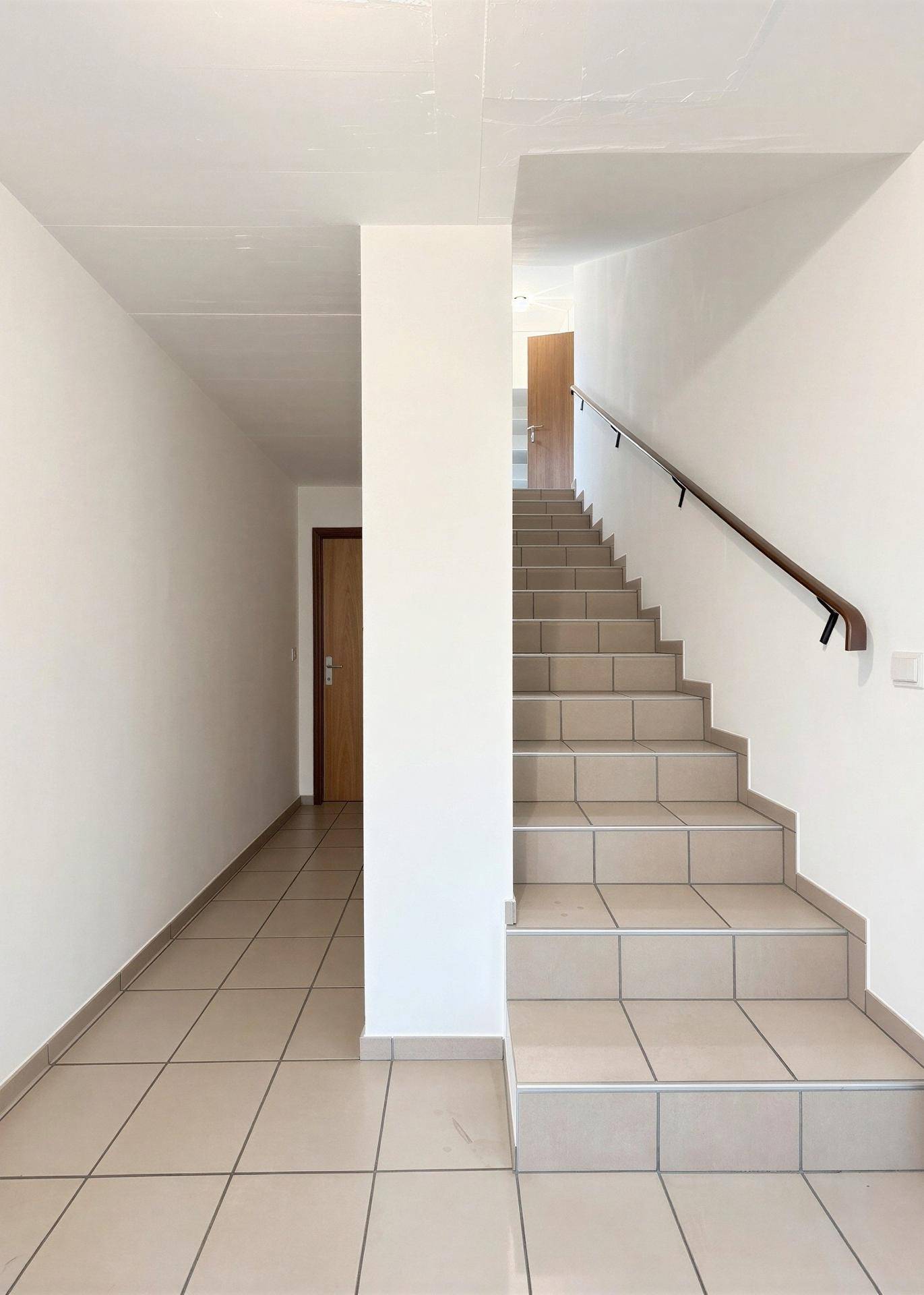 Heller Flur mit Treppenaufgang und Fliesenboden.