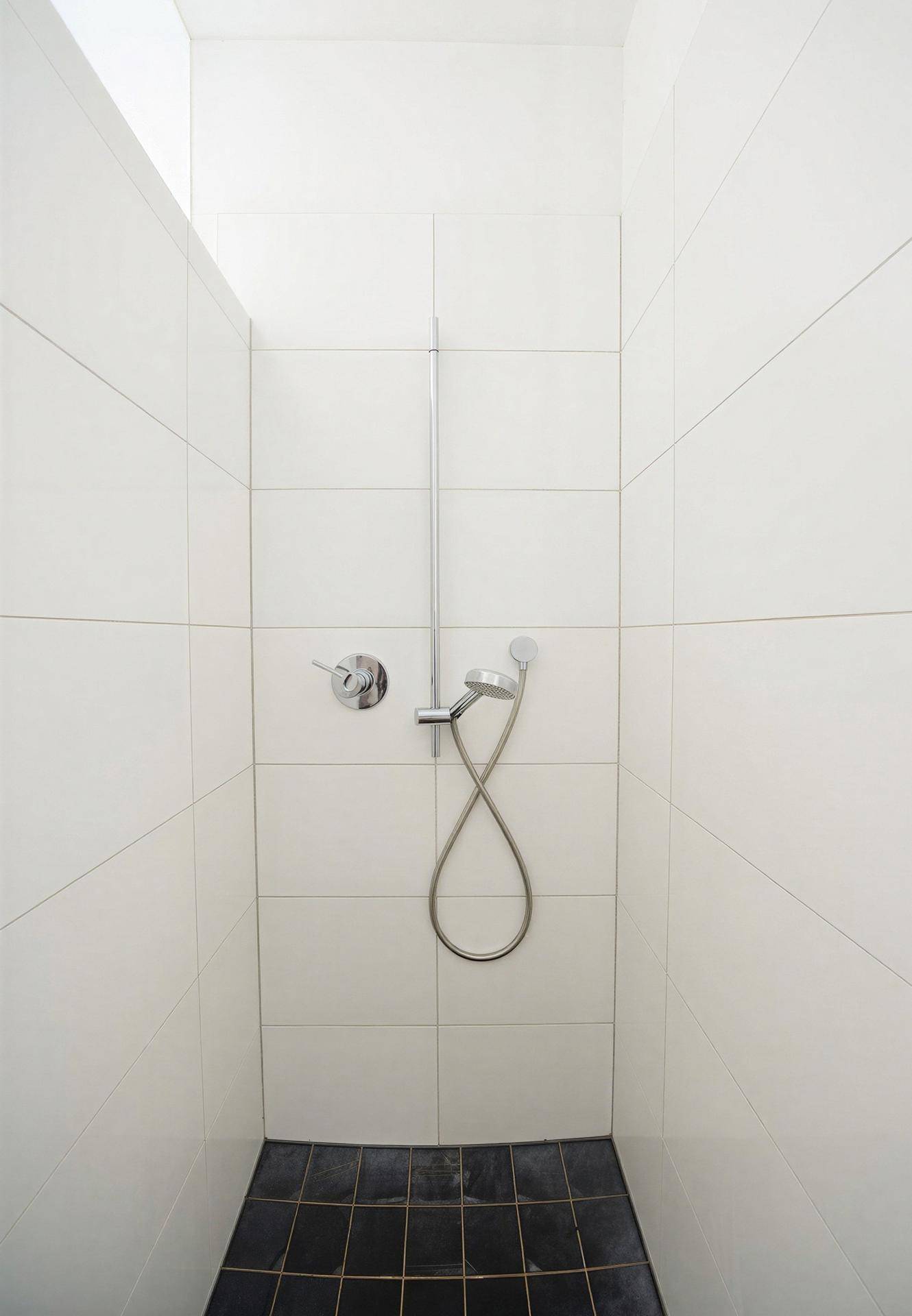 Moderne Duschkabine mit weißen Fliesen und dunklem Boden, minimalistisch gestaltet.