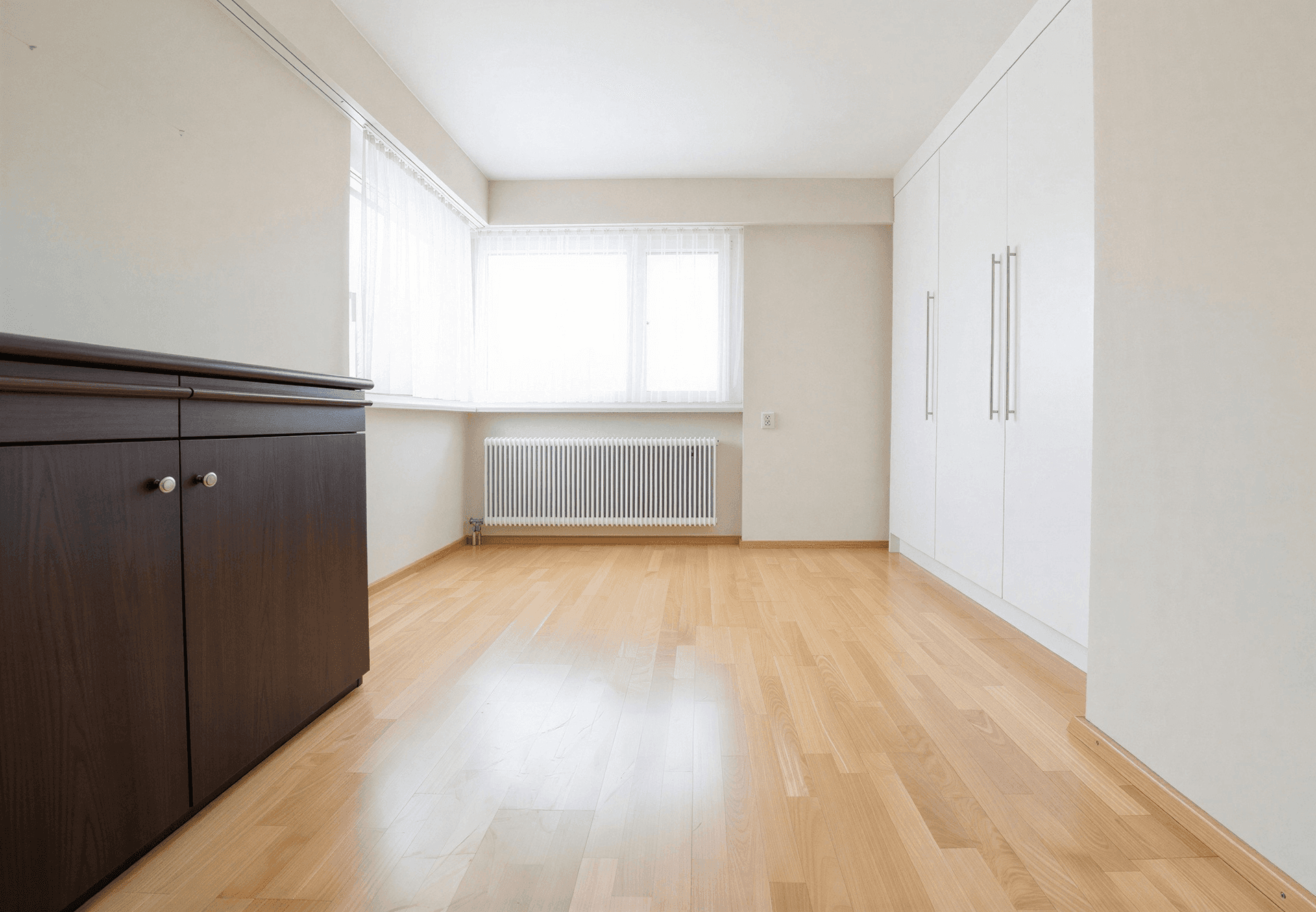 Leeres Zimmer mit hellem Holzboden, Einbauschränken und großem Fenster.