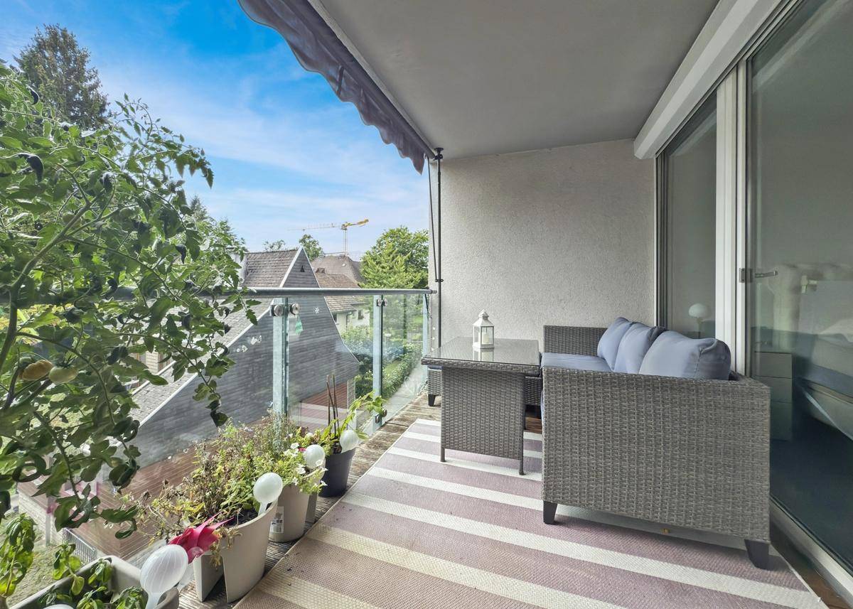 Möblierter Balkon mit Glasbrüstung und Blick auf die Umgebung und Berge.