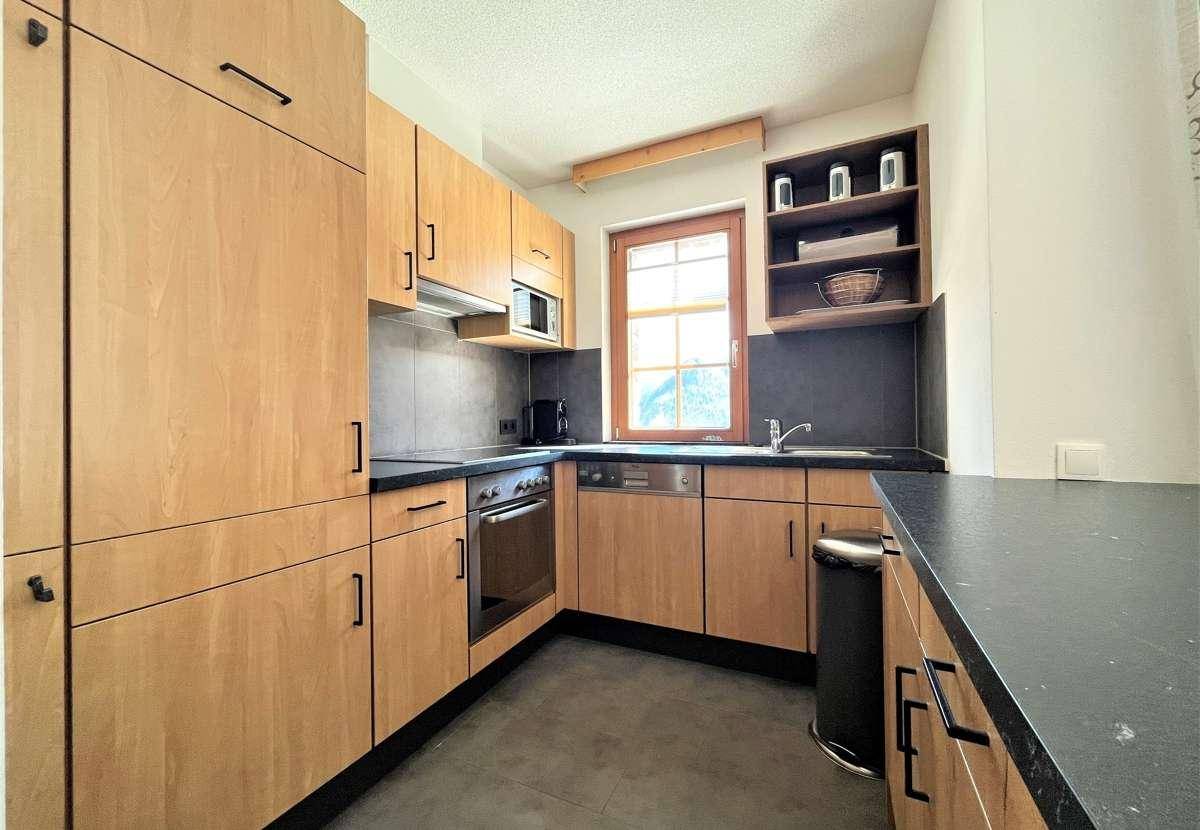 Funktionale Küche mit Holzschränken, dunkler Arbeitsplatte und Fenster.