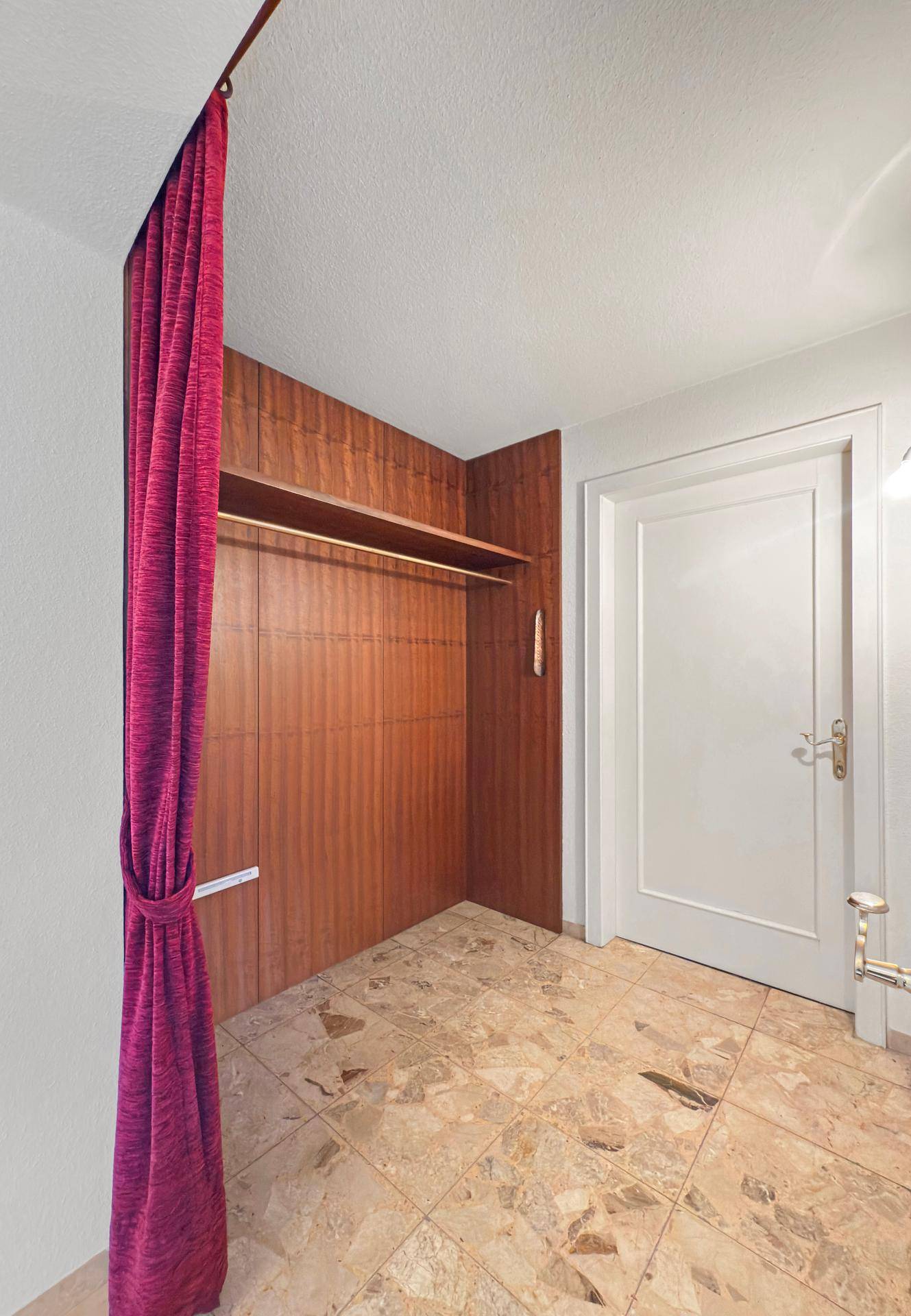 Kleiner Raum mit Holzwandverkleidung und Vorhang, möglicherweise als Ankleidebereich genutzt.