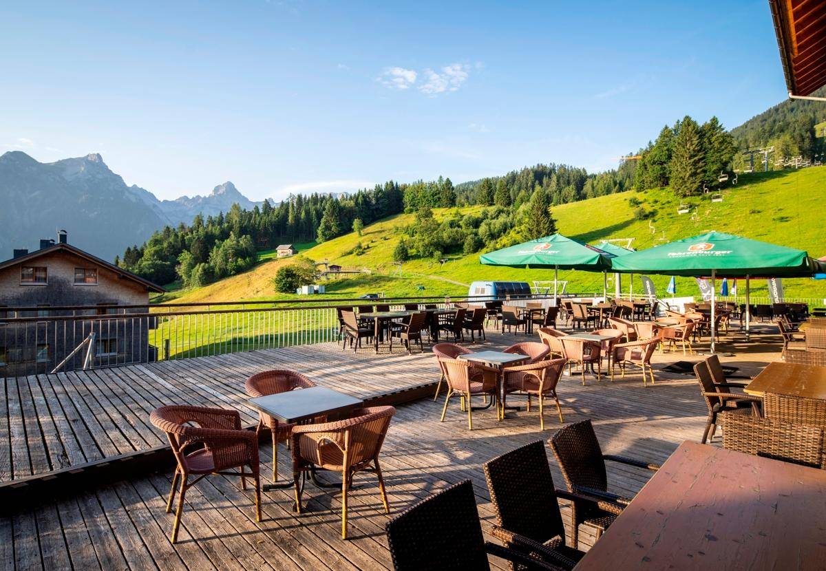 Große Holzterrasse mit vielen Sitzgelegenheiten und Blick auf die grüne Berglandschaft.