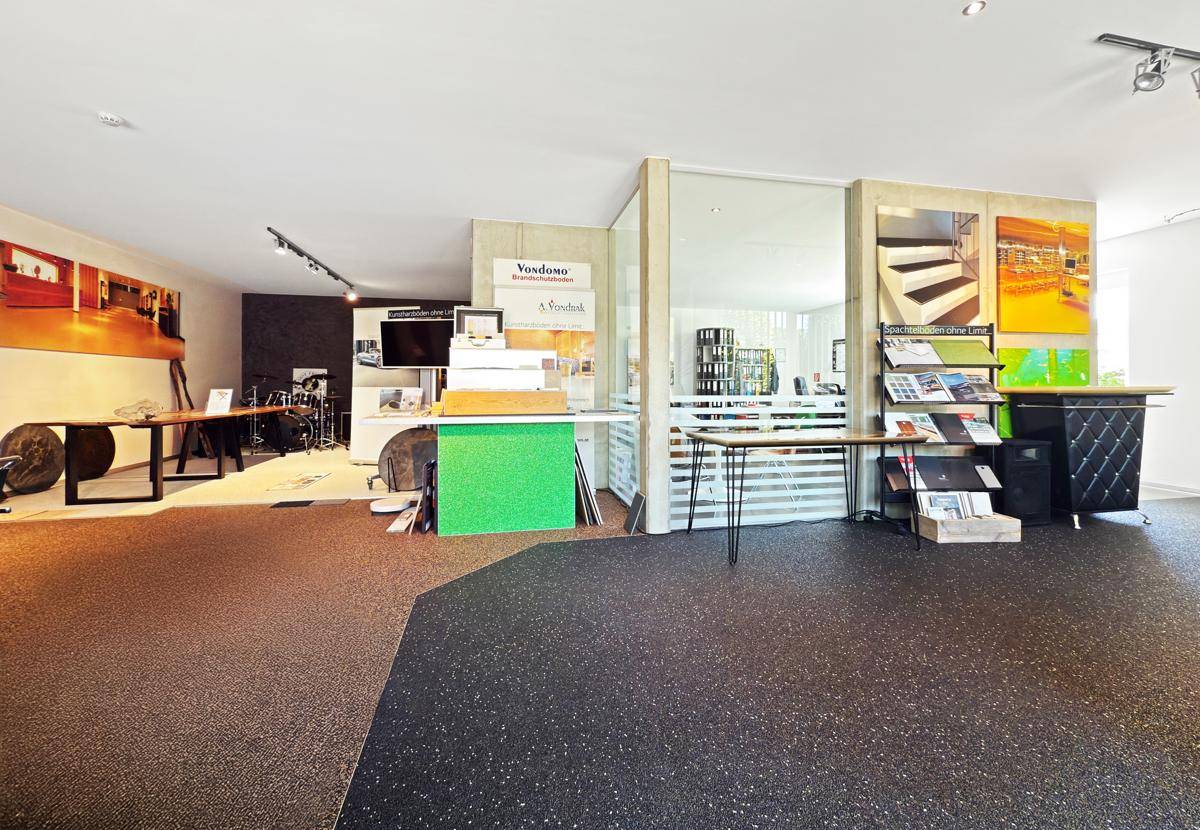 Moderner Ausstellungsbereich mit verschiedenen Bodenmustern, Produktpräsentationen und einer Glaswand.