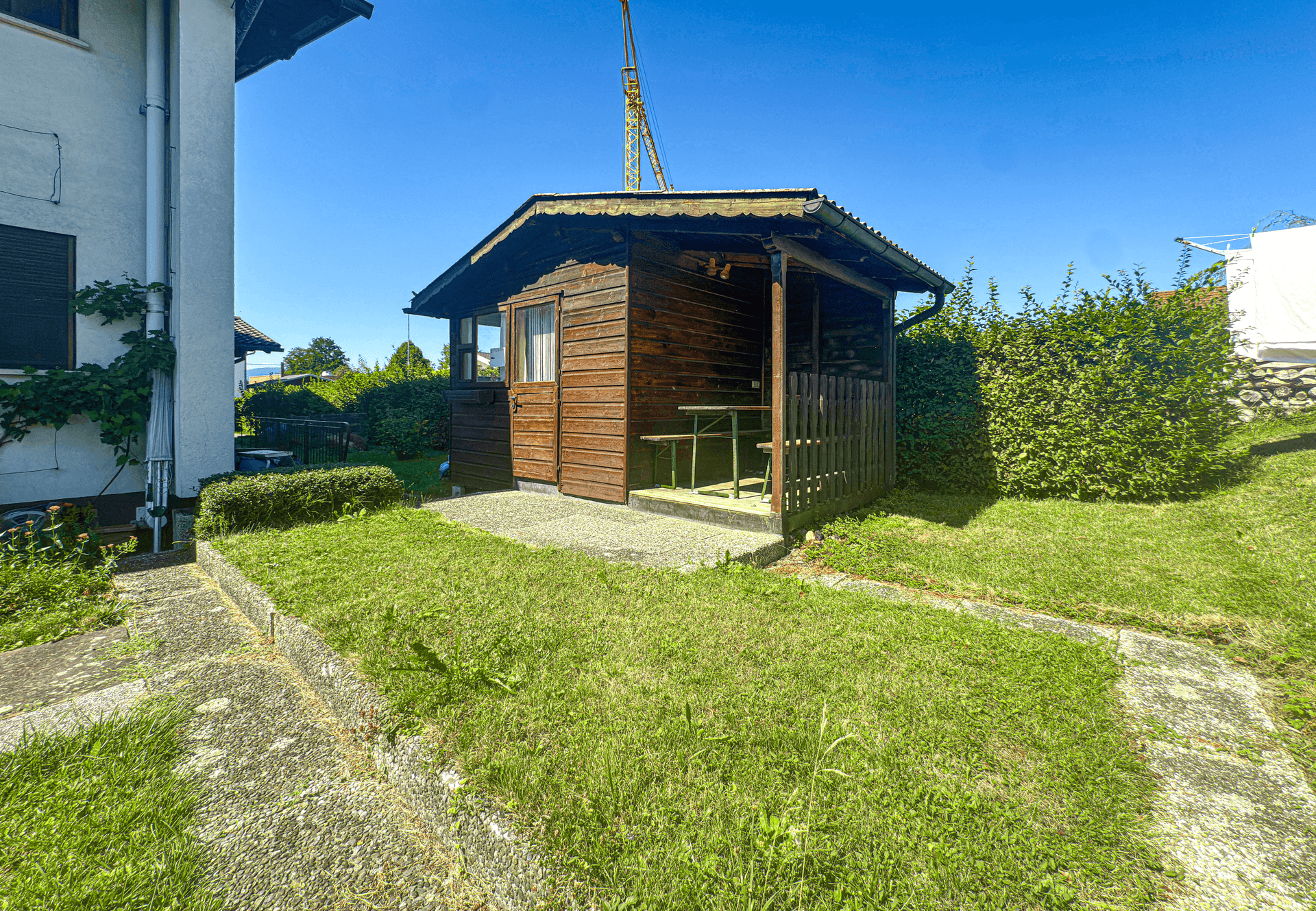 Rustikales Gartenhaus aus Holz mit kleiner Veranda und Sitzgelegenheit im Grünen.