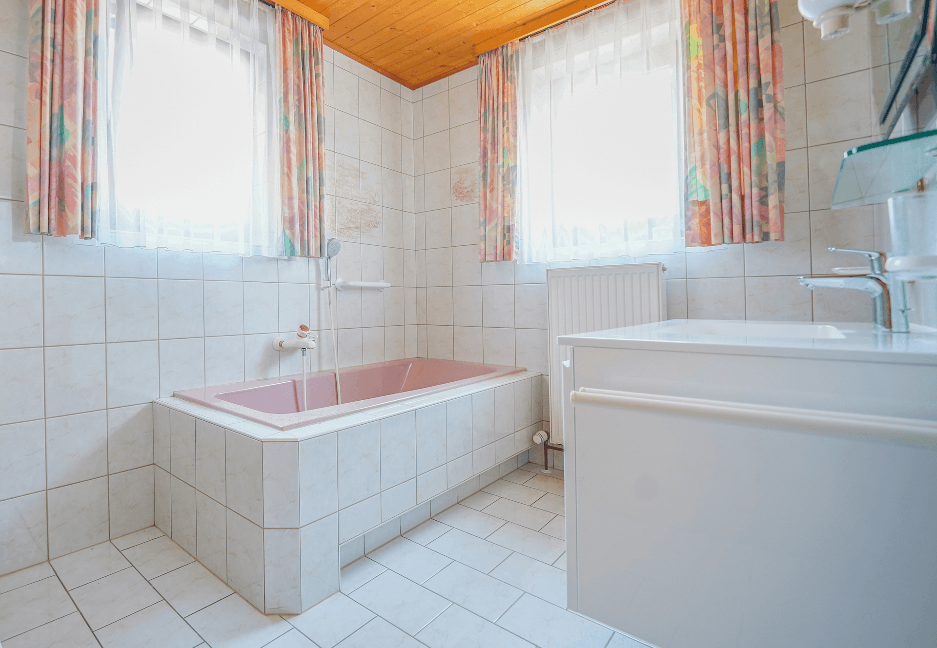 Badezimmer mit Badewanne, Fliesenwänden und Holzdecke, in einem älteren Stil.