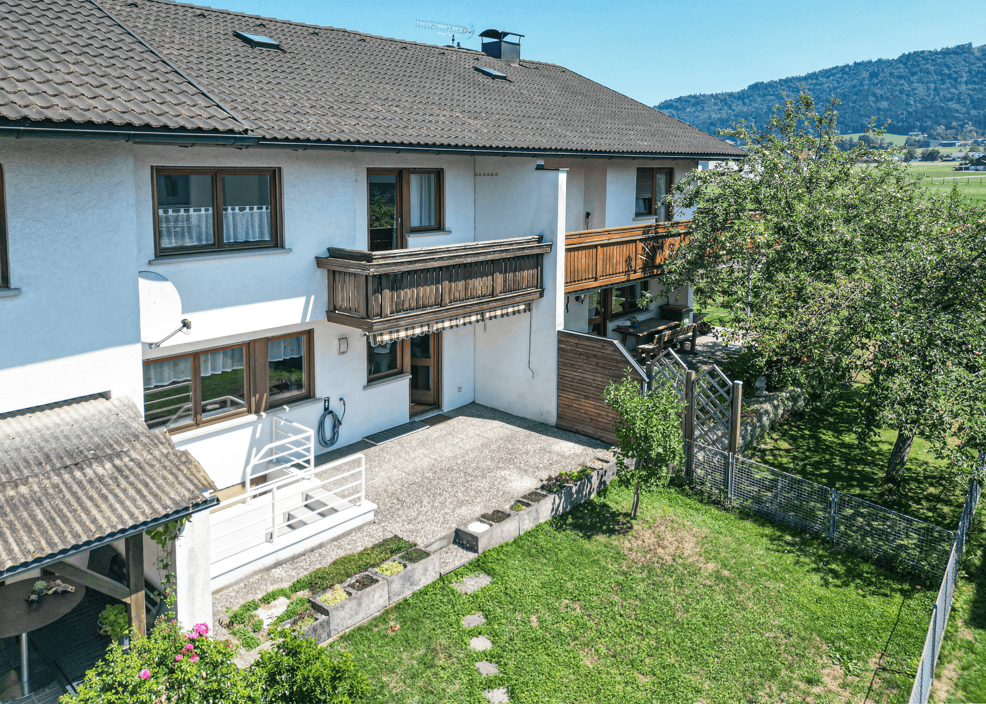 Luftaufnahme des Hauses mit Garten, Terrasse und Bergblick im Hintergrund.