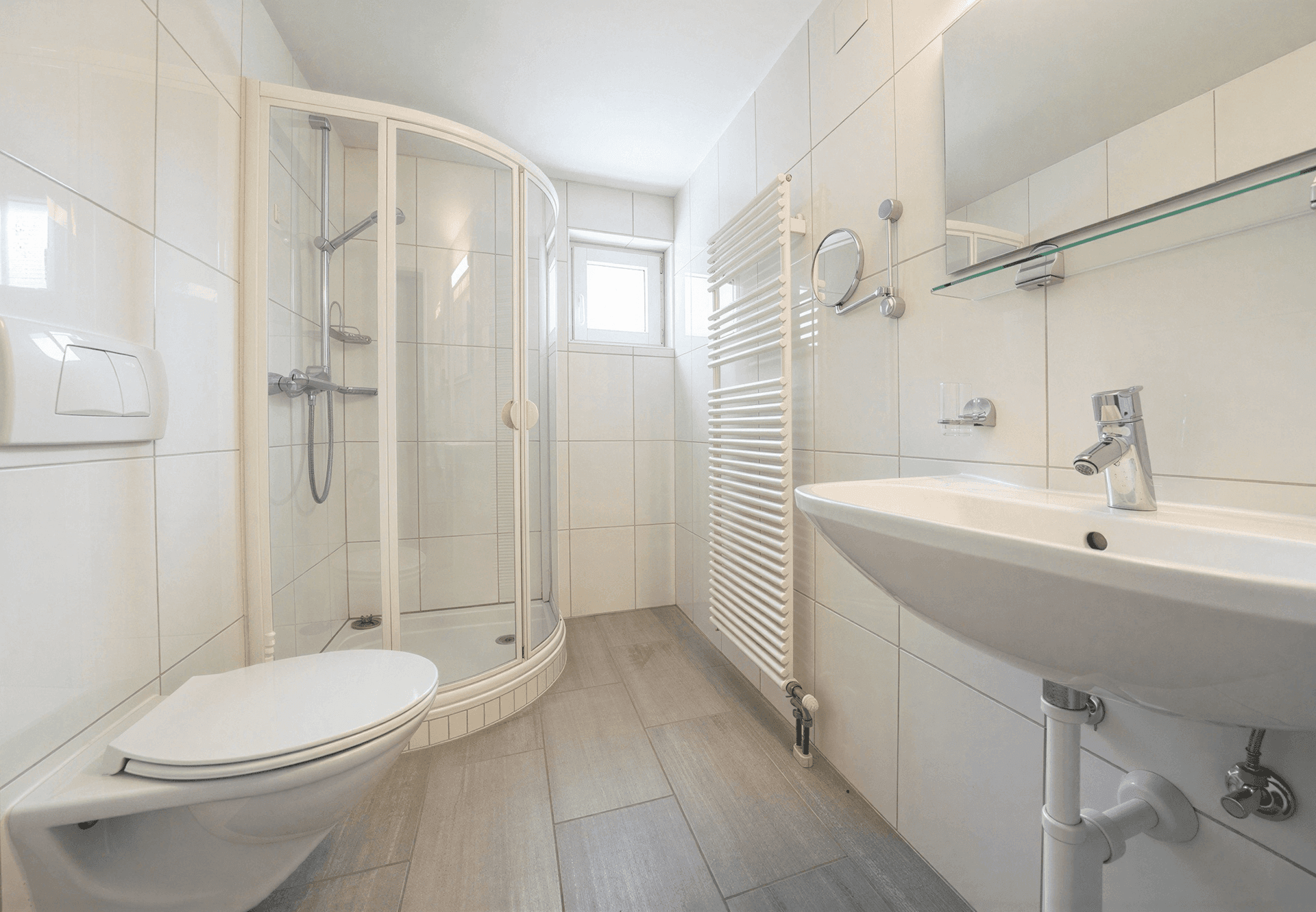 Helles Badezimmer mit Duschkabine, Waschbecken und beheiztem Handtuchhalter.