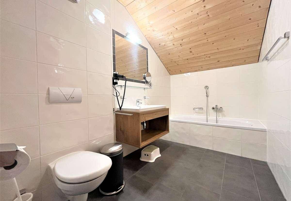 Helles Badezimmer mit Badewanne, WC und Einzelwaschbecken, ausgestattet mit modernen Fliesen und Holzdecke.