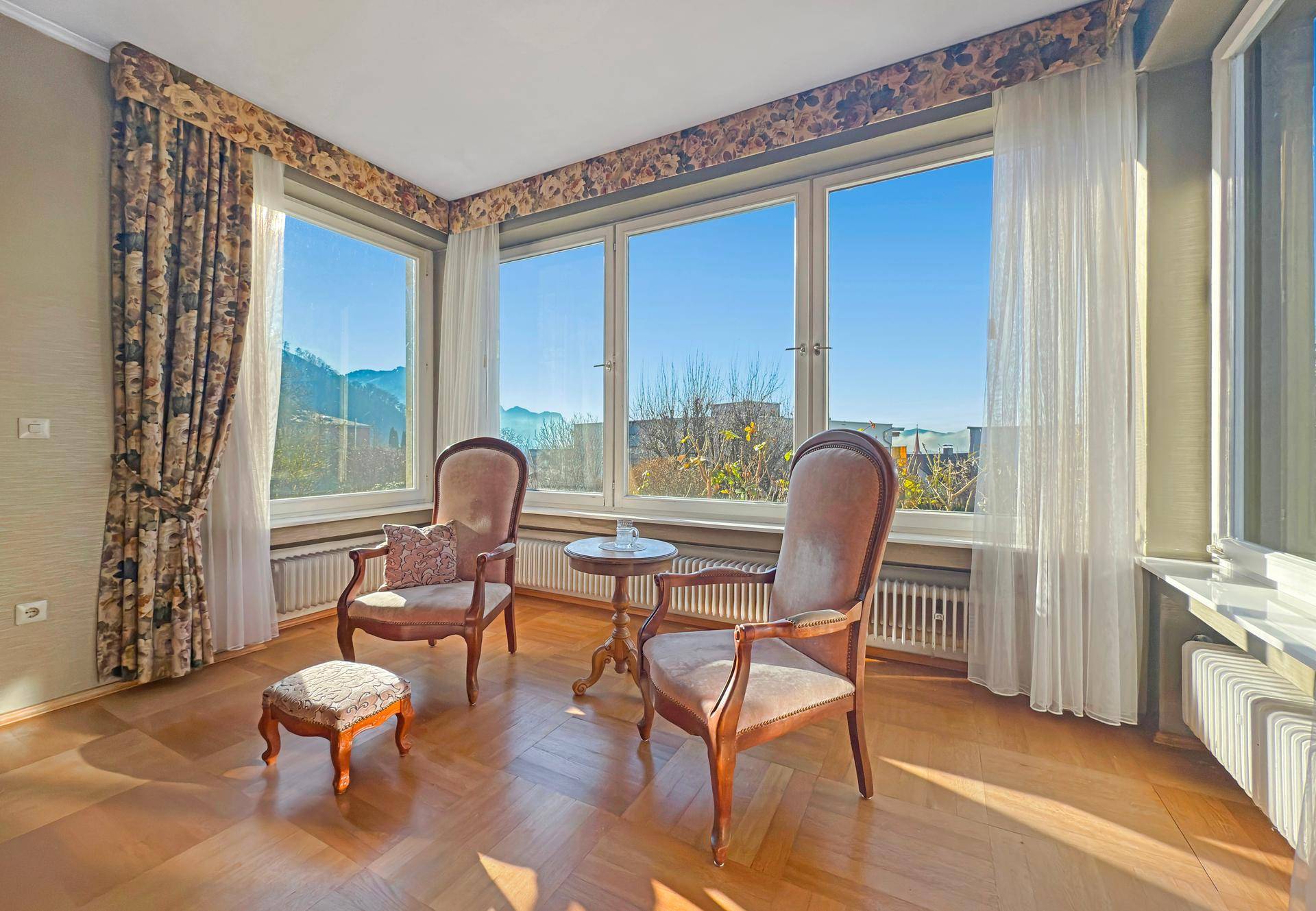 Gemütliche Sitzecke mit großen Fenstern, die viel Tageslicht hereinlassen und eine weite Aussicht bieten.