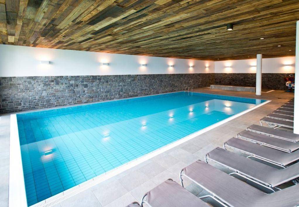 Großes Hallenbad mit Liegestühlen und Holzdecke, ideal zur Entspannung nach dem Skifahren.